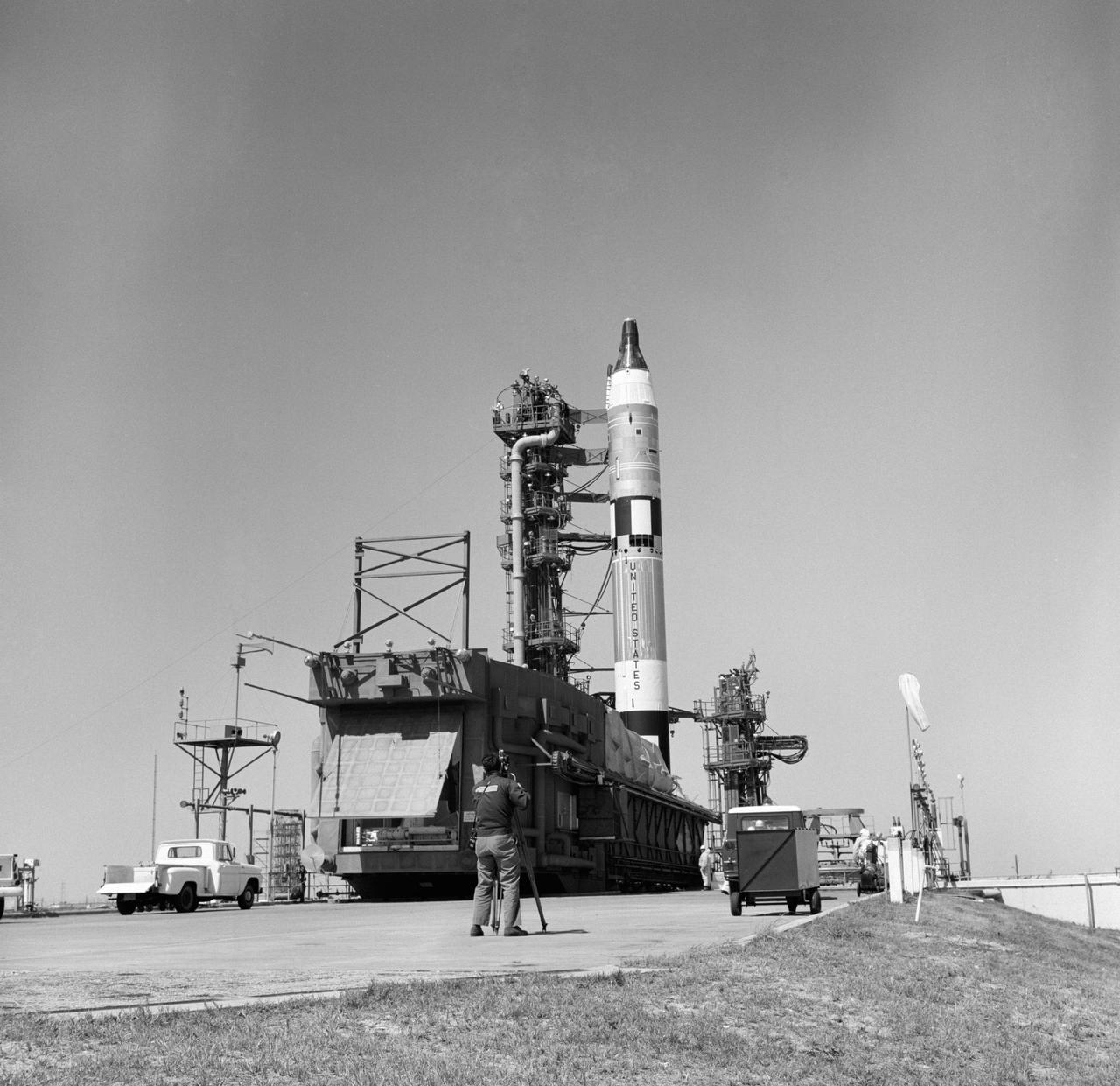 S65-21881 (1965) --- Overall view of the Gemini-Titan 3 on Launch Pad 19, with erector lowered. The GT-3 liftoff was at 9:24 a.m. (EST) on March 23, 1965. A photographer stands at bottom of launch pad with a movie camera.