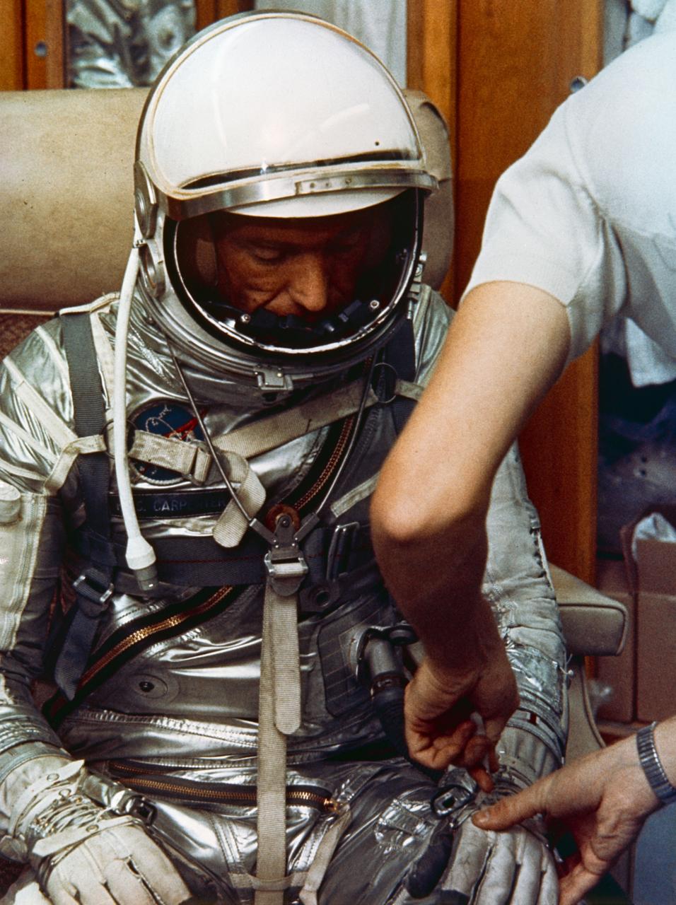 S65-24622 (May 1962) --- Astronaut M. Scott Carpenter, prime pilot for the Mercury-Atlas 7 (MA-7) flight, is seen in Hangar S crew quarters during a suiting exercise. He is assisted in suiting by technician Al Rochford. In this view, Carpenter is fully suited and is having his gloves adjusted. Photo credit: NASA