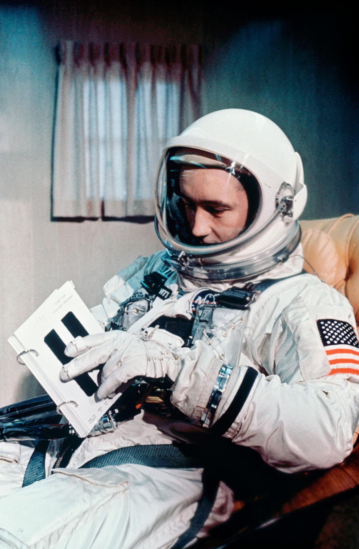 Jim McDivitt wears his spacesuit while reviewing a crew procedures book prior to launch