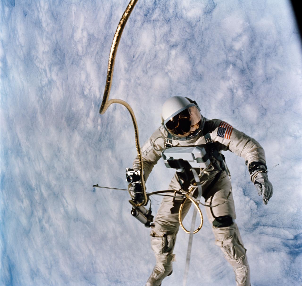 S65-30427 (3 June 1965) --- Astronaut Edward H. White II, pilot for the Gemini-Titan 4 (GT-4) spaceflight, floats in the zero-gravity of space during the third revolution of the GT-4 spacecraft. White wears a specially designed spacesuit. His face is shaded by a gold-plated visor to protect him from unfiltered rays of the sun. In his right hand he carries a Hand-Held Self-Maneuvering Unit (HHSMU) that gives him control over his movements in space. White also wears an emergency oxygen chest pack; and he carries a camera mounted on the HHSMU for taking pictures of the sky, Earth and the GT-4 spacecraft. He is secured to the spacecraft by a 25-feet umbilical line and a 23-feet tether line. Both lines are wrapped together in gold tape to form one cord. Astronaut James A. McDivitt, command pilot, remained inside the spacecraft during the extravehicular activity (EVA). Photo credit: NASA    EDITOR'S NOTE: Astronaut Edward H. White II died in the Apollo/Saturn 204 fire at Cape Kennedy on Jan. 27, 1967.
