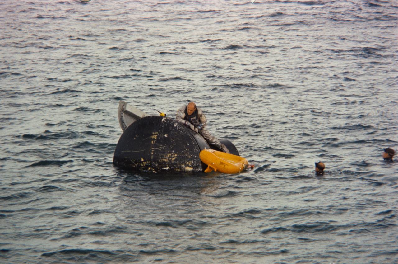 S65-43954 (23 Aug. 1965) --- Astronaut Thomas P. Stafford, Gemini-6 prime crew pilot, climbs out of a boilerplate model of a Gemini spacecraft during water egress training in the Gulf of Mexico. A NASA swimmer in the water nearby assists in the exercise.