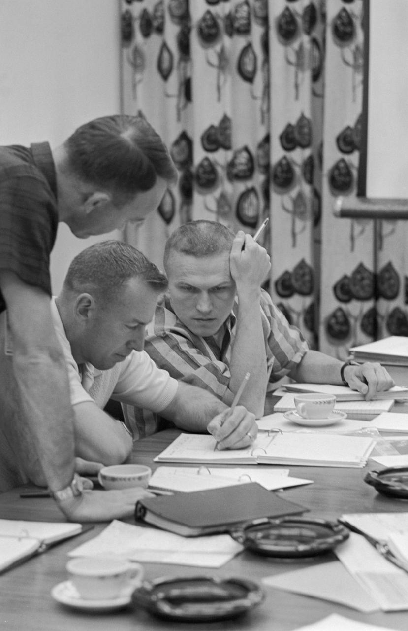 S65-56313 (2 Dec. 1965) --- Gemini-7 astronauts James Lovell Jr. (center) and Frank Borman (right) review mission requirements for their Gemini-7 flight. The two astronauts are scheduled for a 14-day mission. On the fifth day, they will attempt a rendezvous with the Gemini-6 spacecraft to be launched nine days later and piloted by astronaut Walter Schirra Jr. and Thomas Stafford. Photo credit: NASA