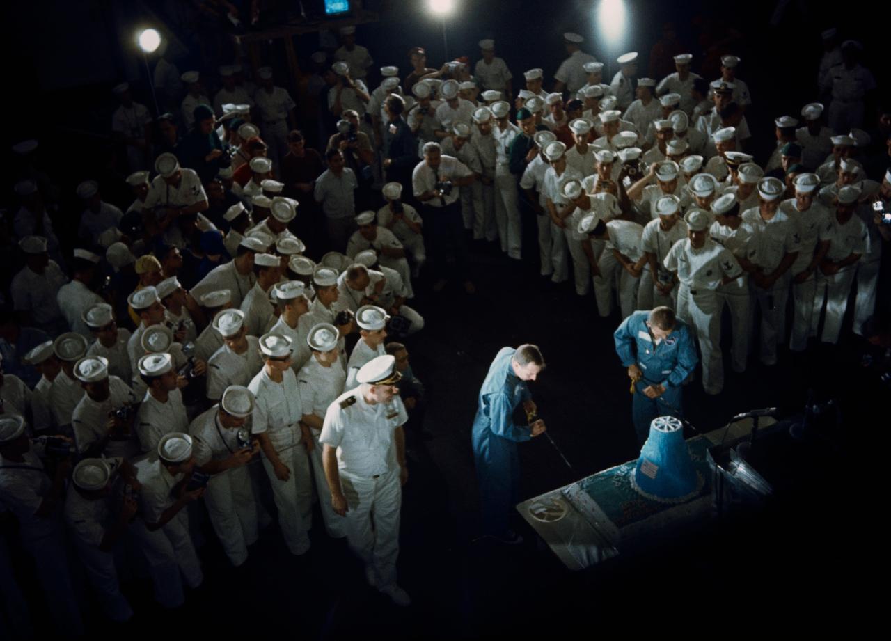 S65-61823 (18 Dec. 1965) --- Astronauts James A. Lovell Jr. (left), Gemini-7 pilot, and Frank Borman (right), command pilot, slice into a huge cake which was part of their warm welcome after arriving aboard the aircraft carrier USS Wasp. The National Aeronautics and Space Administration's Gemini-7 spacecraft splashed down in the Western Atlantic recovery area at 9:05 a.m. (EST), Dec. 18, 1965, to conclude a highly successful 14-day mission in space. Sailors gather around close to watch the cake cutting. Photo credit: NASA