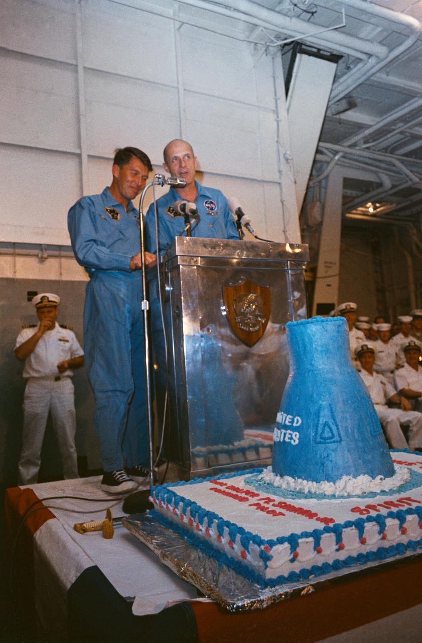 S65-61825 (16 Dec. 1965) --- Astronauts Walter M. Schirra Jr. (left), command pilot, and Thomas P. Stafford, pilot, speak to crewmen onboard the aircraft carrier USS Wasp after successful recovery of the Gemini-6 spacecraft. Note the cake with a model of the Gemini spacecraft in its center, which is positioned in front of the astronauts. Photo credit: NASA or National Aeronautics and Space Administration