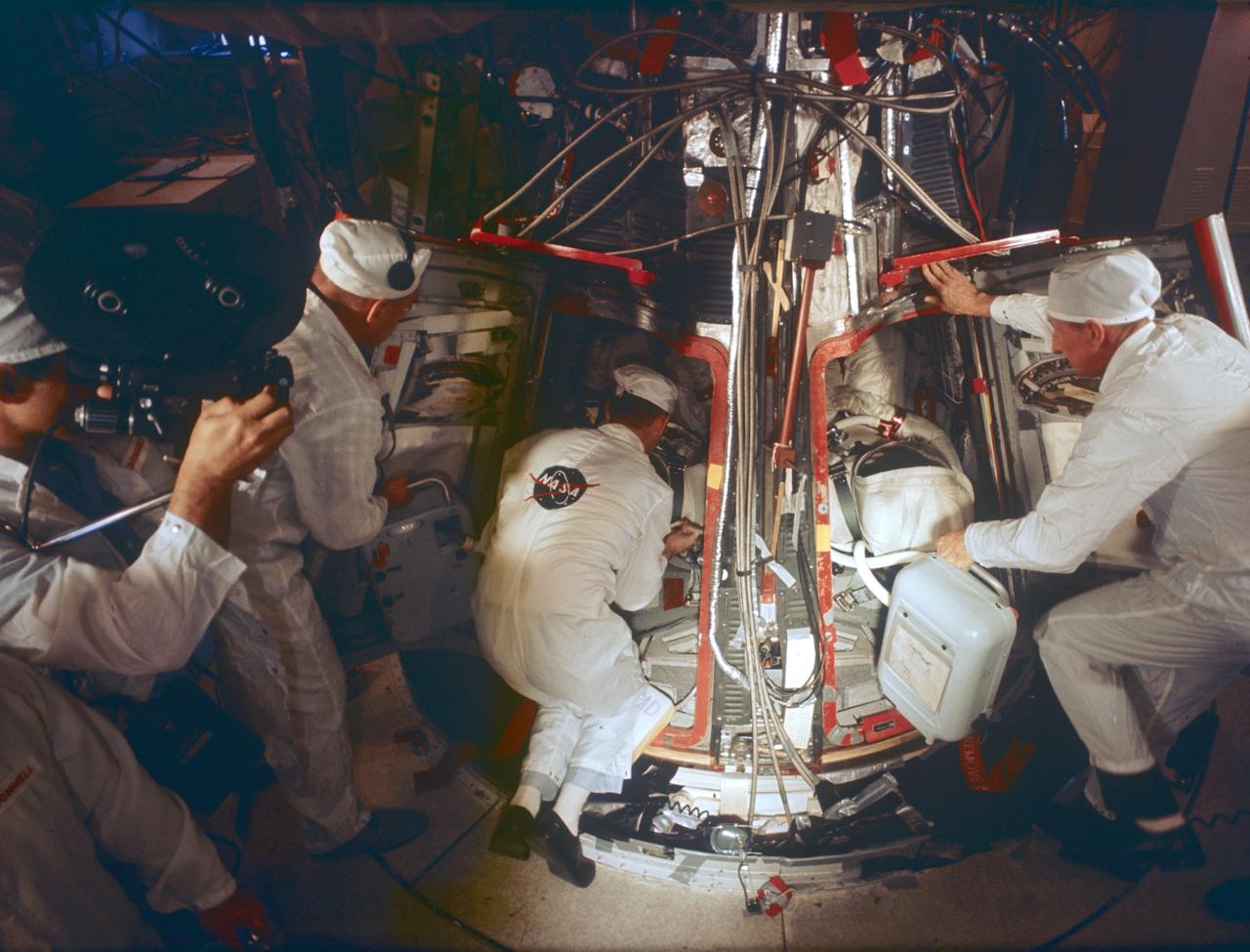 S65-61835 (15 Nov. 1965) --- Technicians assist the prime crew for the Gemini-7 spaceflight in systems checks inside their spacecraft in the White Room atop Pad 19. Prime crew members are astronauts Frank Borman (left, inside spacecraft), command pilot, and James A. Lovell Jr. (right, inside spacecraft), pilot. They wear the new light-weight spacesuit planned for use during their 14-day mission. Photo credit: NASA