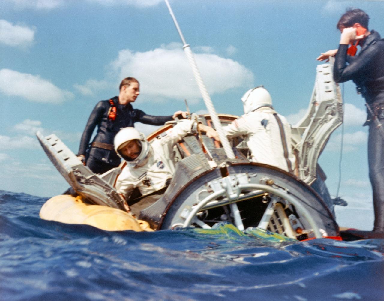S65-61886 (16 Dec. 1965) --- A water level view of Navy divers assisting Gemini-6 crew members Stafford and Schirra to open hatches after landing in the Atlantic. Photo credit: NASA or National Aeronautics and Space Administration