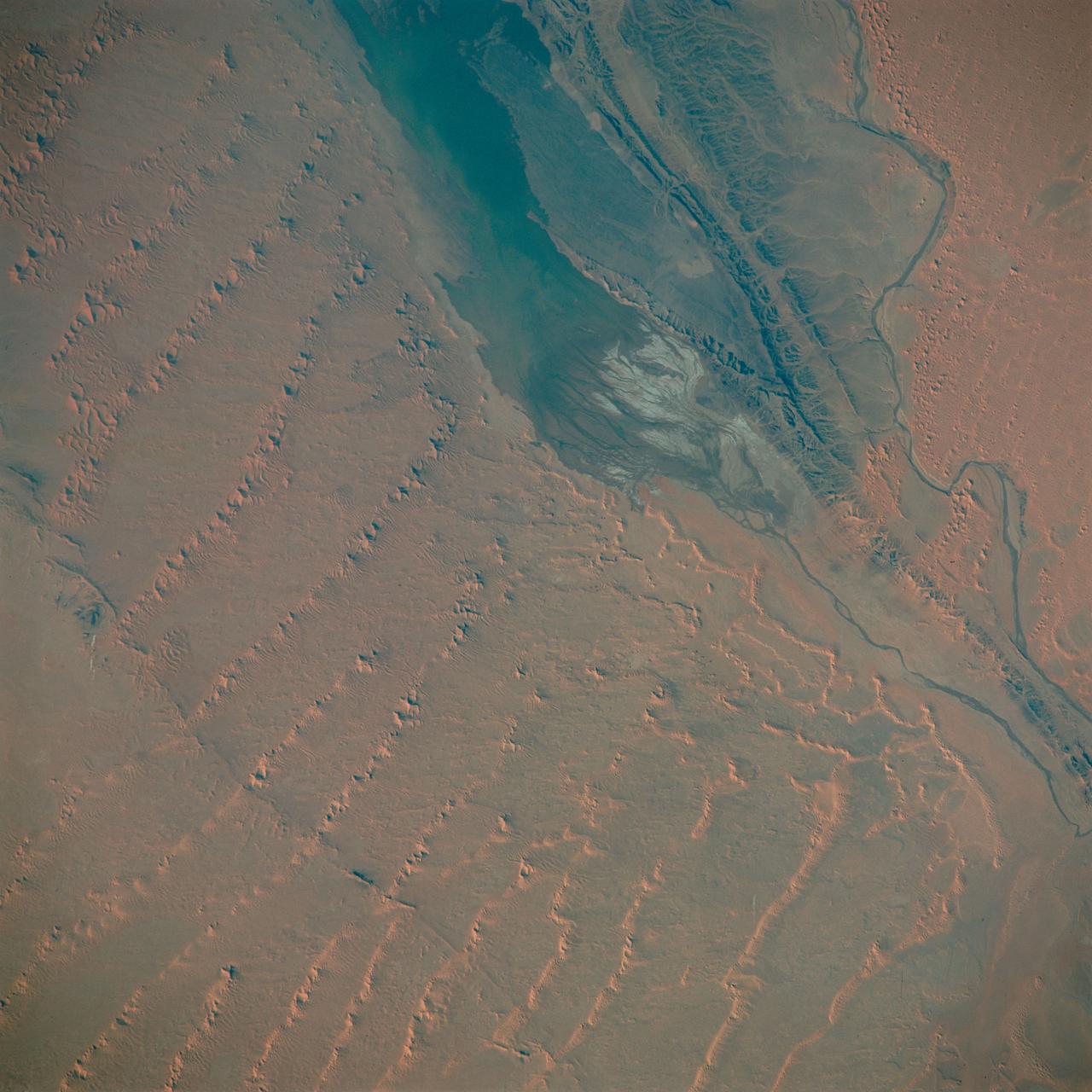 S65-63830 (5 Dec. 1965) --- Algeria, south-southeast of the Colomb Bechar area, as seen from the National Aeronautics and Space Administration's Gemini-7 spacecraft. Sand dunes are 200 to 300 feet high in the Grand Erg Occidental area. The Quod Sacura River can be seen in the upper left corner. The white spot in the middle of the picture is the Sebcha el Malah salt beds. It should be noted that the area had just experienced very heavy rains (first in many years) and the stream and salt flat are inundated. This photograph was taken with a modified 70mm Hasselblad camera, with Eastman Kodak, Ektachrome MS (S.O. 217) color film. Photo credit: NASA