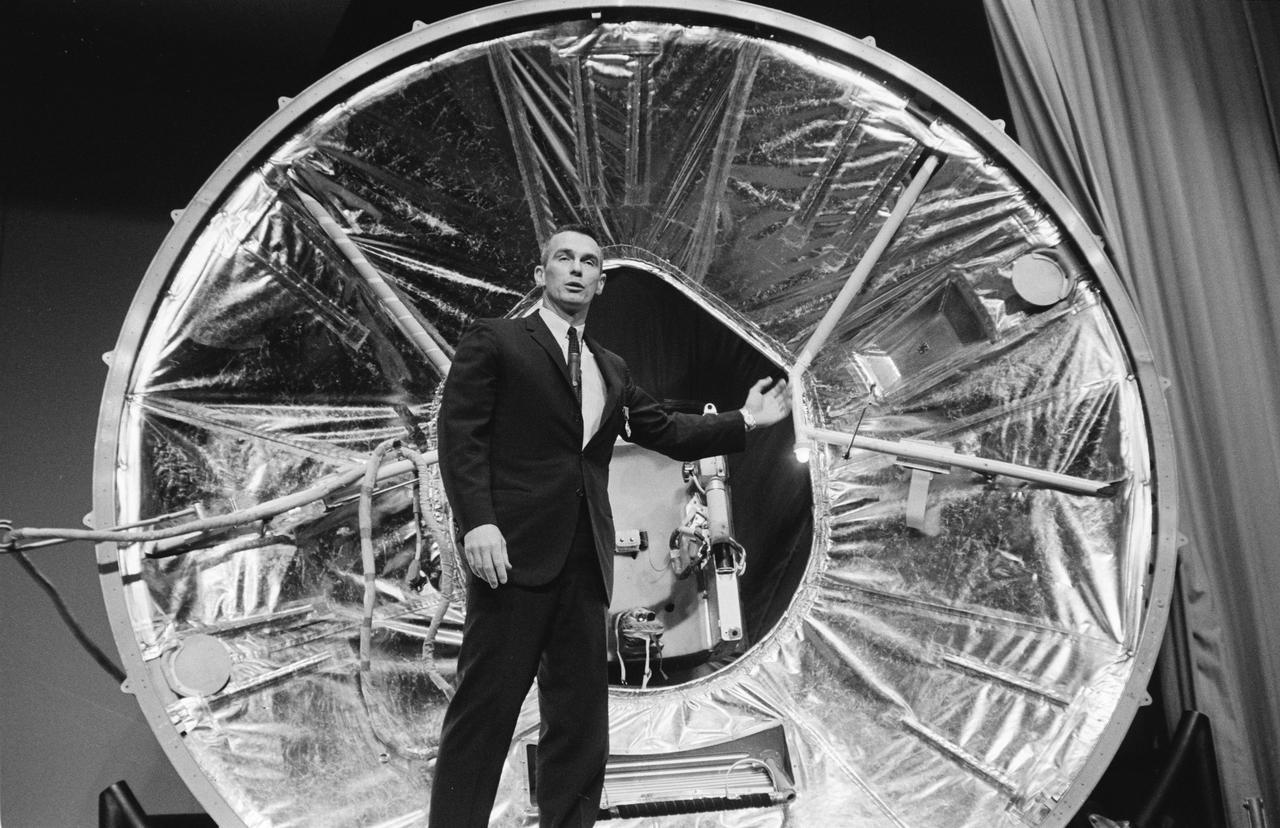 S66-32698 (17 June 1966) --- Astronaut Eugene A. Cernan discusses his Gemini-9A extravehicular activity before a gathering of news media representatives in the MSC auditorium. In the background is an Astronaut Maneuvering Unit (AMU) mock-up mounted in a mock-up of a Gemini spacecraft adapter equipment section. Astronauts Cernan and Thomas P. Stafford completed their three-day mission in space on June 6, 1966. Photo credit: NASA