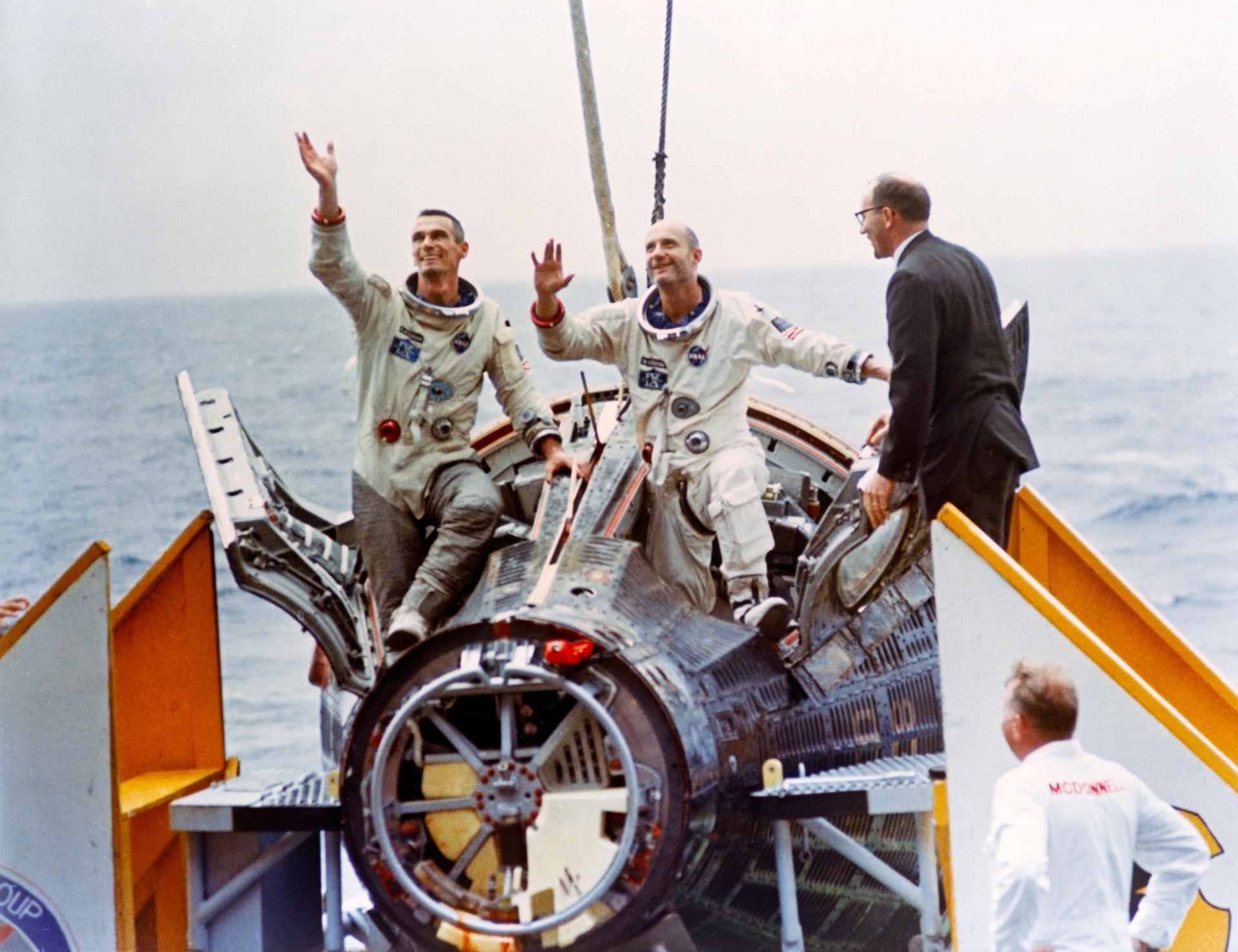 Astronauts Thomas Stafford (right) and Eugene Cernan wave to the crowd aboard the aircraft carrier USS Wasp as they emerge from their Gemini-9 capsule. John C. Stonesifer (far right), with the Manned Spacecraft Center's Landing and Recovery Division, was onboard to greet the astronauts.