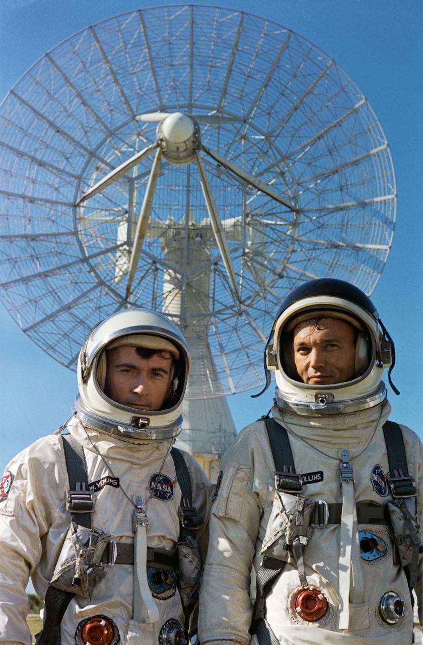 S66-42725 (16 July 1966) --- Astronauts John W. Young (left), command pilot, and Michael Collins, pilot, the Gemini-10 prime crew during a photo session for the press outside the Kennedy Space Center (KSC) Mission Control Center. Both men are wearing their spacesuits including helmets. Behind them is a large radar dish. Photo credit: NASA