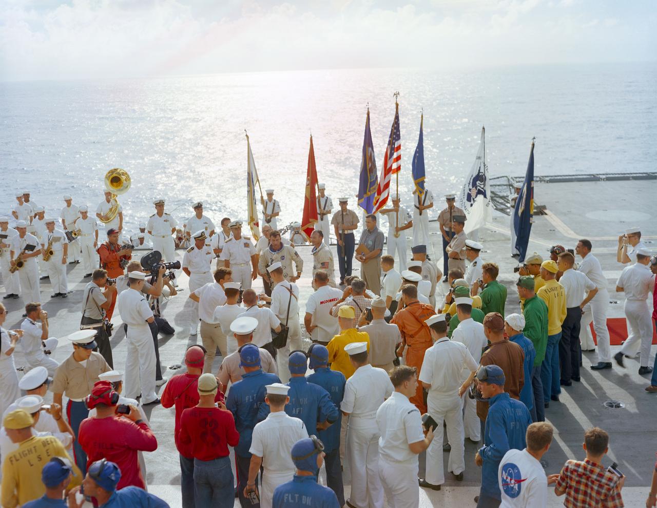 S66-42780 (21 July 1966) --- The crew of the Gemini-10 spaceflight, astronaut John W. Young (left), command pilot, and Michael Collins, pilot, talk on live radio and television during welcome aboard ceremonies on the deck of the USS Guadalcanal. The astronauts were picked up from the ocean, following a successful splashdown, by a recovery helicopter and flown to the Guadalcanal to begin postflight medical and technical debriefings. Photo credit: NASA