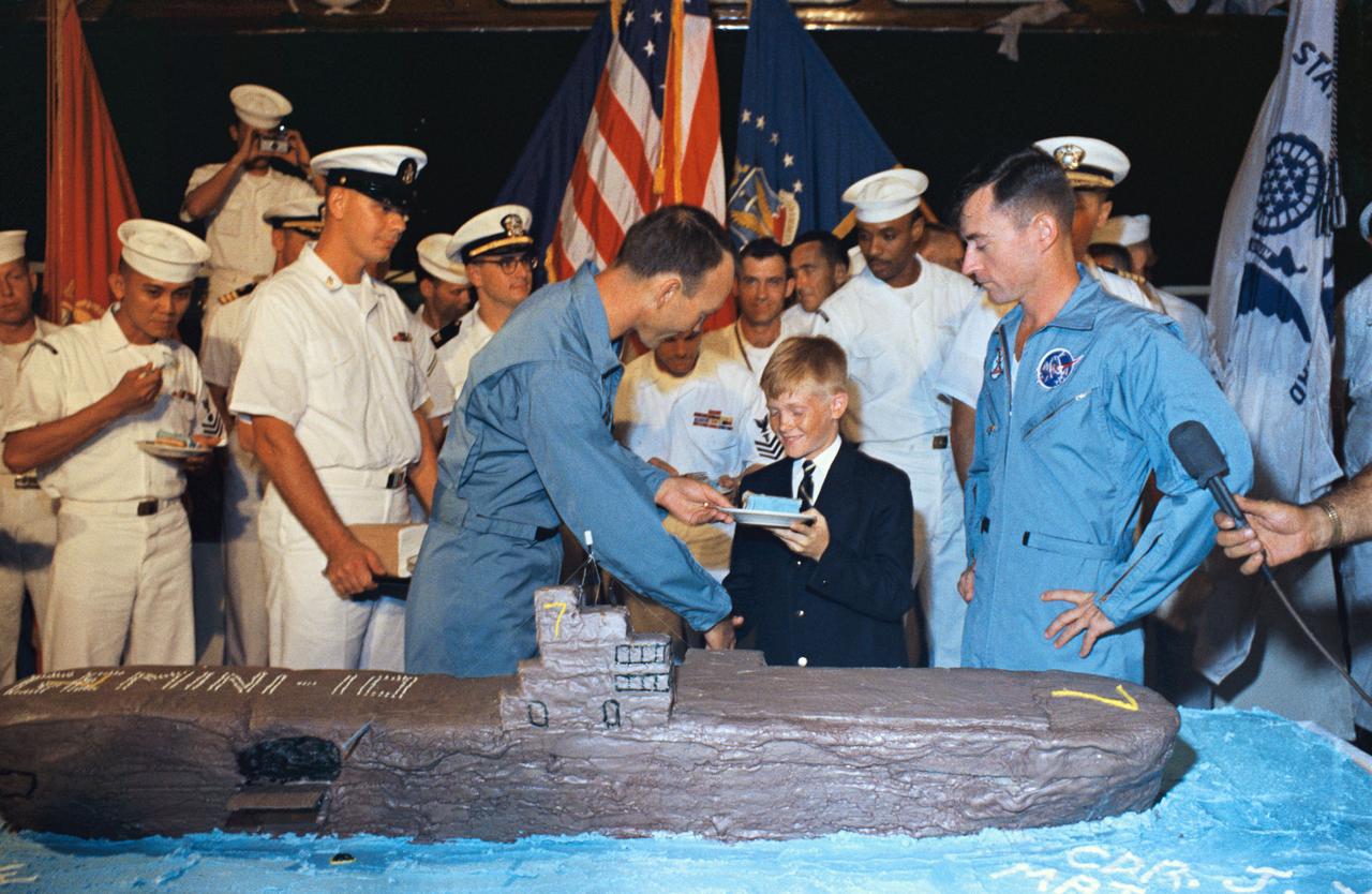 S66-42787 (21 July 1966) --- Twelve-year -old Billy Doyle of Virginia Beach, VA., shakes hands with astronaut Michael Collins, Gemini-10 pilot, aboard the recovery ship USS Guadalcanal. At right is John W. Young, command pilot of the Gemini-10 spaceflight. Billy represented 41 youngsters permitted aboard the Guadalcanal to witness the recovery with their Naval fathers or close relatives, marking the first time dependents have been permitted aboard a ship during a Gemini recovery operation. Photo credit: NASA