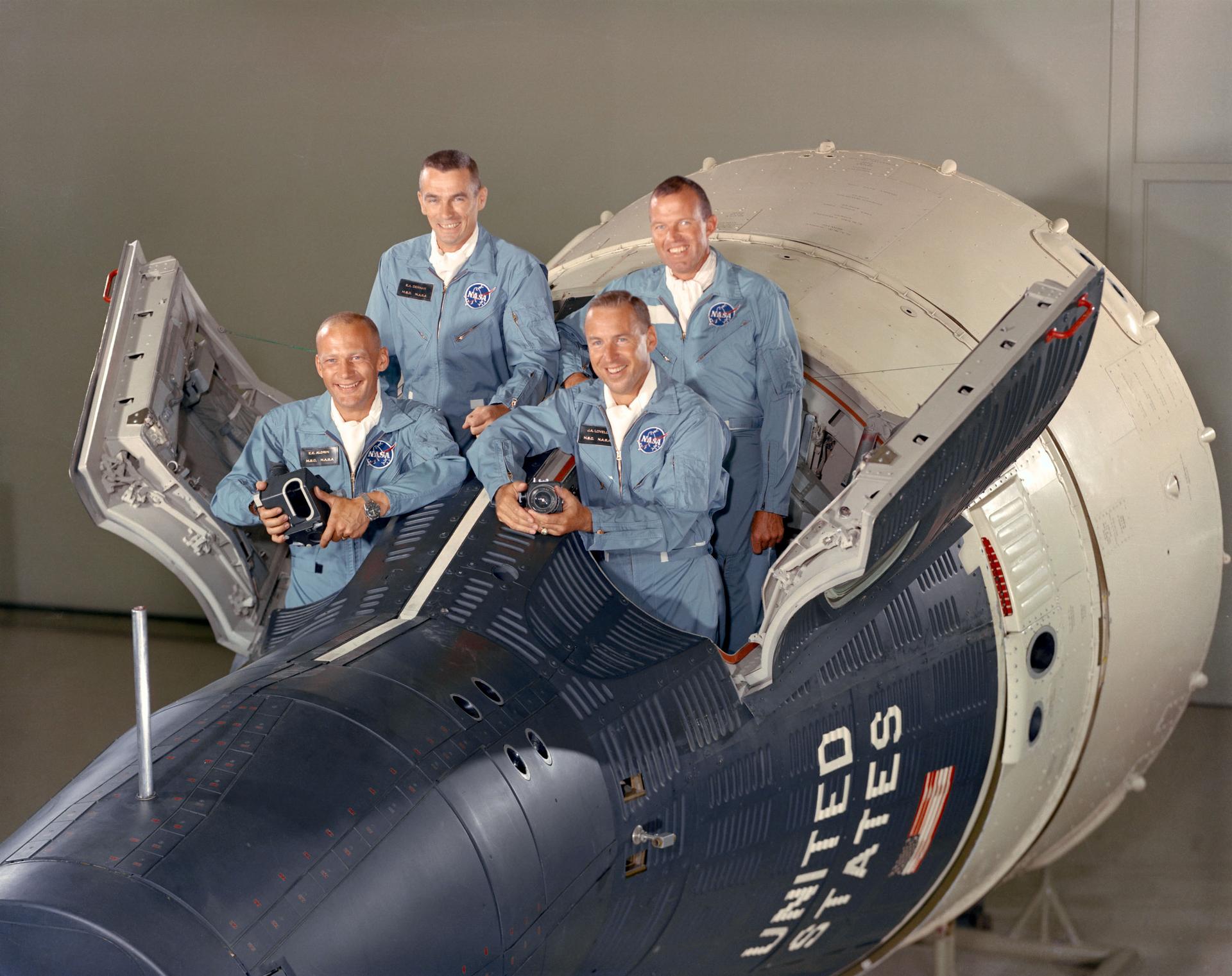 The prime and backup crews for Gemini 12 pose standing inside a Gemini capsule with its hatch doors open.