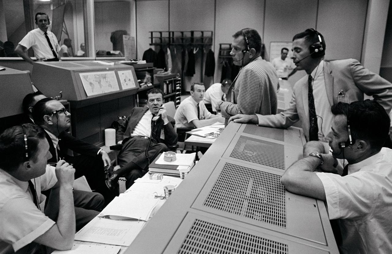 S66-52157 (12 Sept. 1966) --- Discussing the Gemini-11 spaceflight in the Mission Control Center are: (left to right) Christopher C. Kraft Jr., (wearing glasses), Director of Flight Operations; Charles W. Mathews (holding phone), Manager, Gemini Program Office; Dr. Donald K. Slayton (center, checked coat), Director of Flight Crew Operations; astronaut William A. Anders, and astronaut John W. Young. Photo credit: NASA