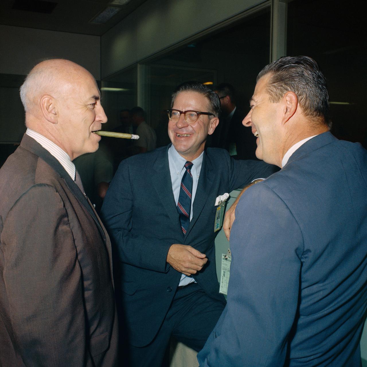 S66-52762 (15 Sept. 1966) --- Dr. Robert R. Gilruth (left) smokes a cigar in Houston's Mission Control Center to celebrate the successful splashdown of Gemini-11. Looking on are James C. Elms (center), MSC deputy director, and Charles W. Mathews, Gemini program manager. Photo credit: NASA