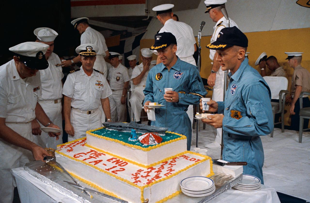 S66-59989 (16 Nov. 1966) --- Gemini-12 astronaut James A. Lovell Jr. (left), command pilot, and Edwin E. Aldrin Jr. (right), pilot, eat a piece of cake presented the two astronauts by crew members of the prime recovery ship, USS Wasp. Gemini-12 splashed down in the Atlantic Ocean at 2:21 p.m. (EST), Nov. 15, 1966, to conclude a four-day mission in space. Photo credit: NASA