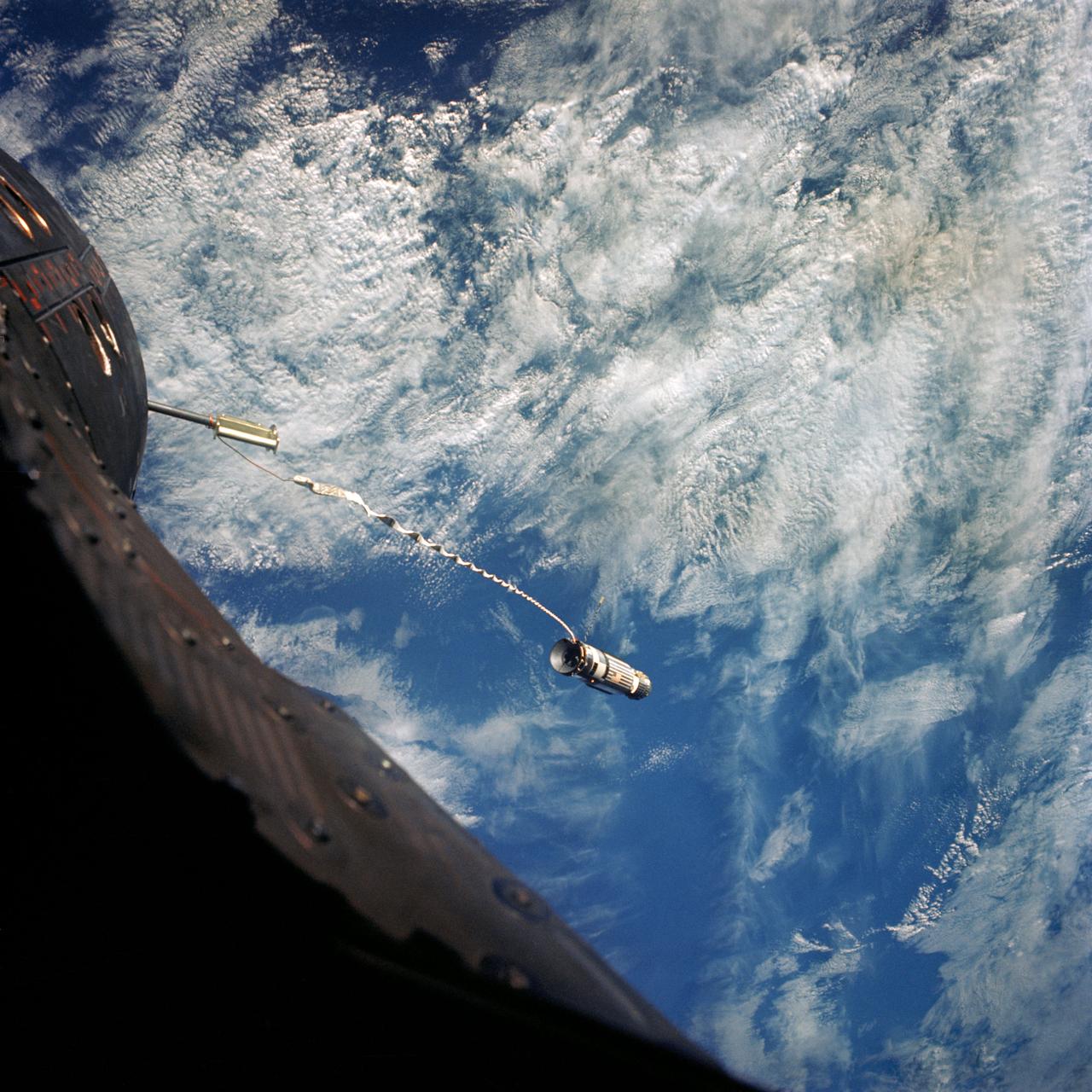 S66-62953 (13 Nov. 1966) --- A 100-foot tether line connects the Agena Target Docking Vehicle with the Gemini-12 spacecraft during its 32nd revolution of Earth. Clouds over the Pacific Ocean are in the background. Photo credit: NASA