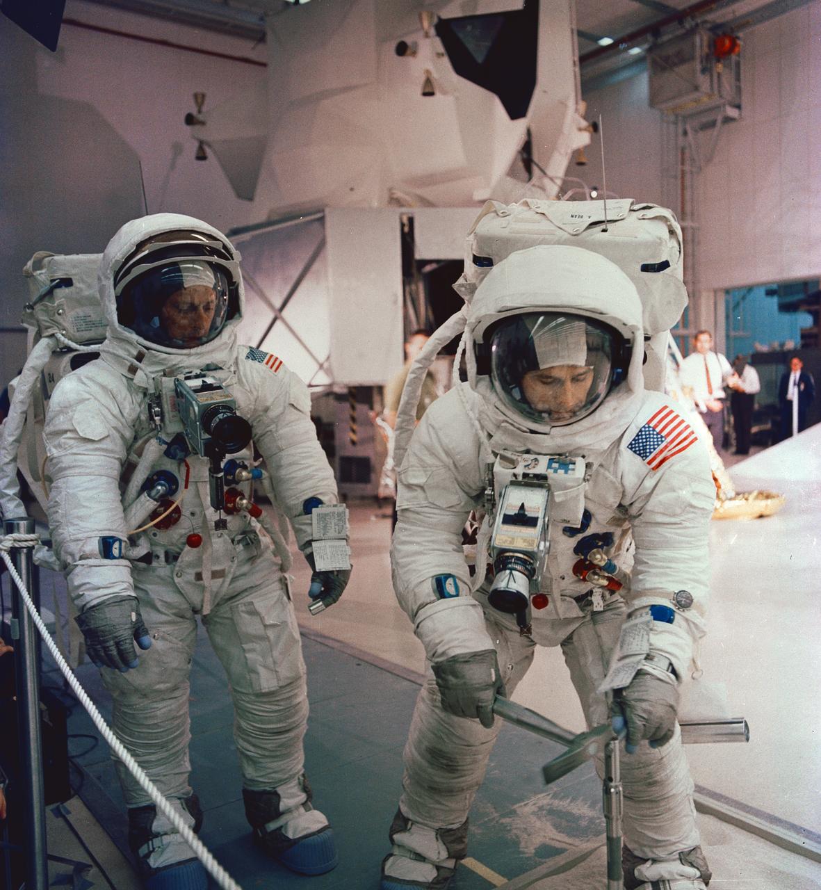 S69-55362 (6 Oct. 1969) --- The two assigned moon-walking crew members for the Apollo 12 lunar landing mission participate in lunar surface extravehicular activity simulations in the Kennedy Space Center's Flight Crew Training Building. Here, astronaut Alan L. Bean, lunar module pilot, simulates driving core tube into lunar surface to obtain a sample. Astronaut Charles Conrad Jr., commander, looks on. A Lunar Module mock-up is in the center background.  Photo credit: NASA or National Aeronautics and Space Administration