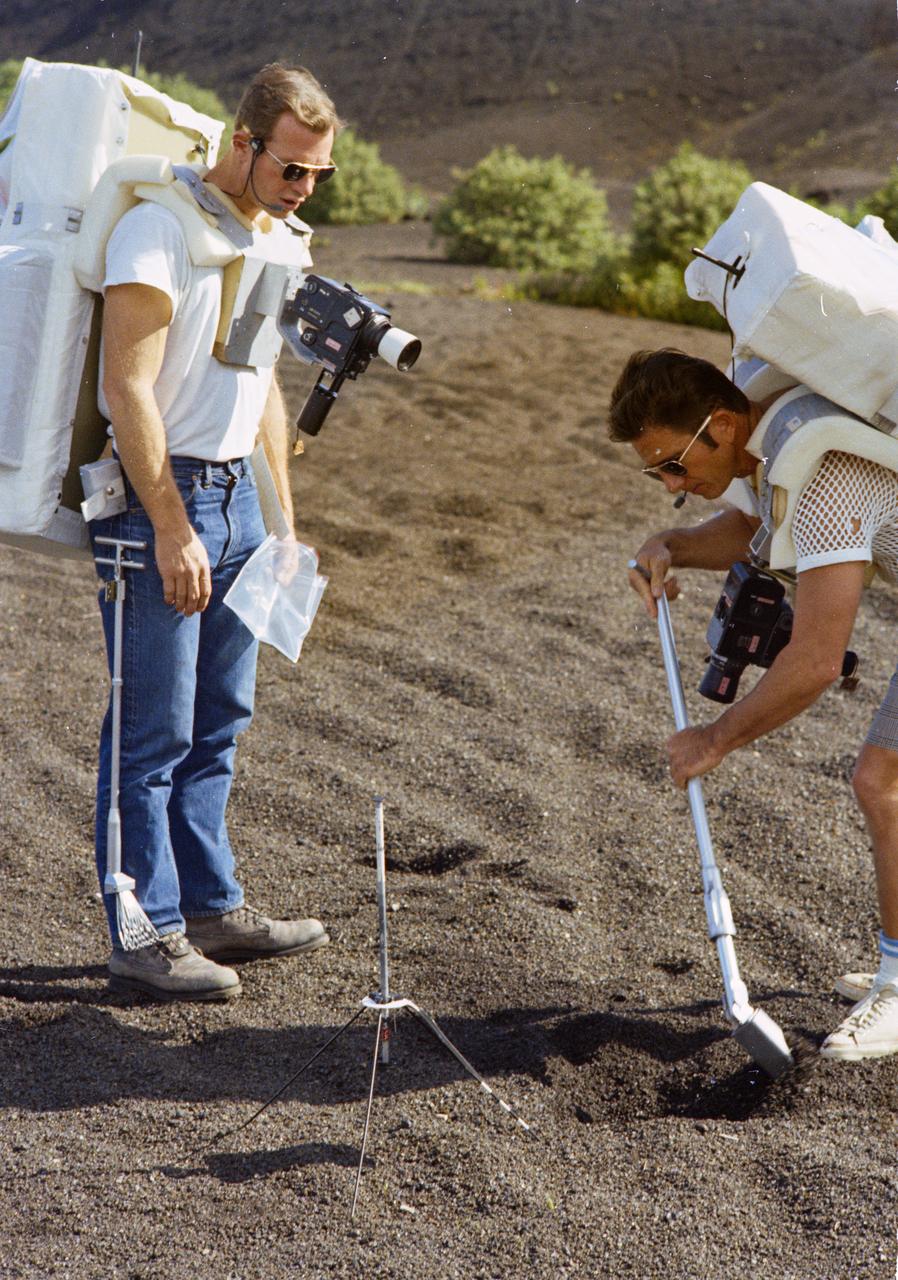 S70-56415 (December 1970) --- At Kapoho, Hawaii, astronauts David R. Scott (left), commander of the Apollo 15 lunar landing mission, and James B. Irwin, lunar module pilot, train at a designated lunar surface simulation area for their upcoming lunar landing mission. Wearing street clothes, but equipped with a Portable Life Support System (PLSS), the two rehearse for a selenological traverse. Here, they are inspecting a grapefruit-sized rock. Photo credit: NASA