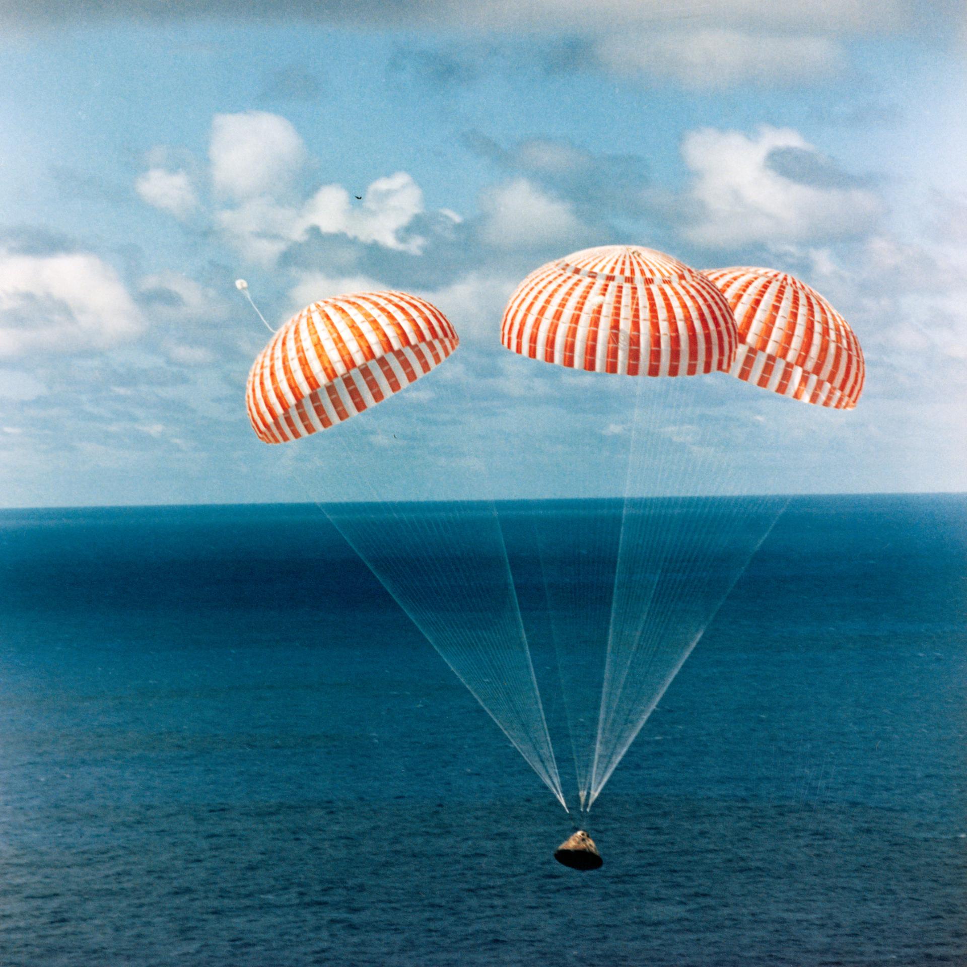 The Apollo 14 dangles from 3 giant red and white parachutes just before splashing down into the South Pacific Ocean.