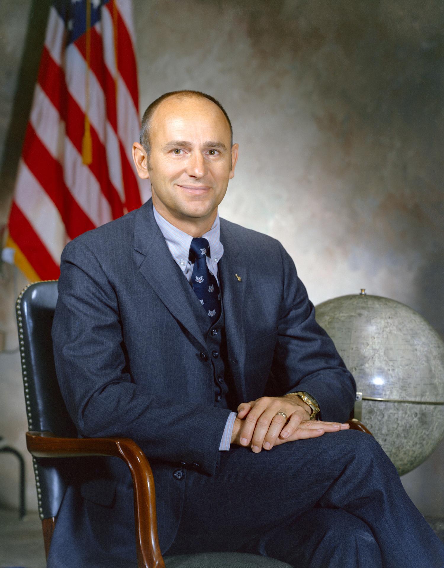 Astronaut Alan Bean sitting in a chair with an American flag and a globe of the moon behind him.