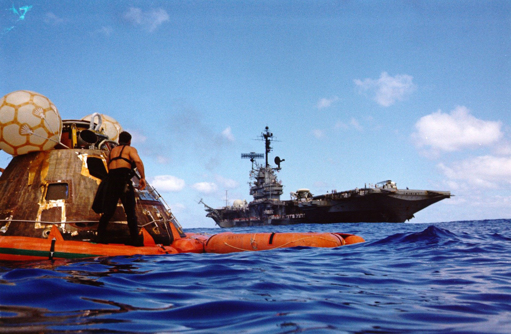 The Apollo 17 command module floats in the foreground with the USS Ticonderoga in the distance.