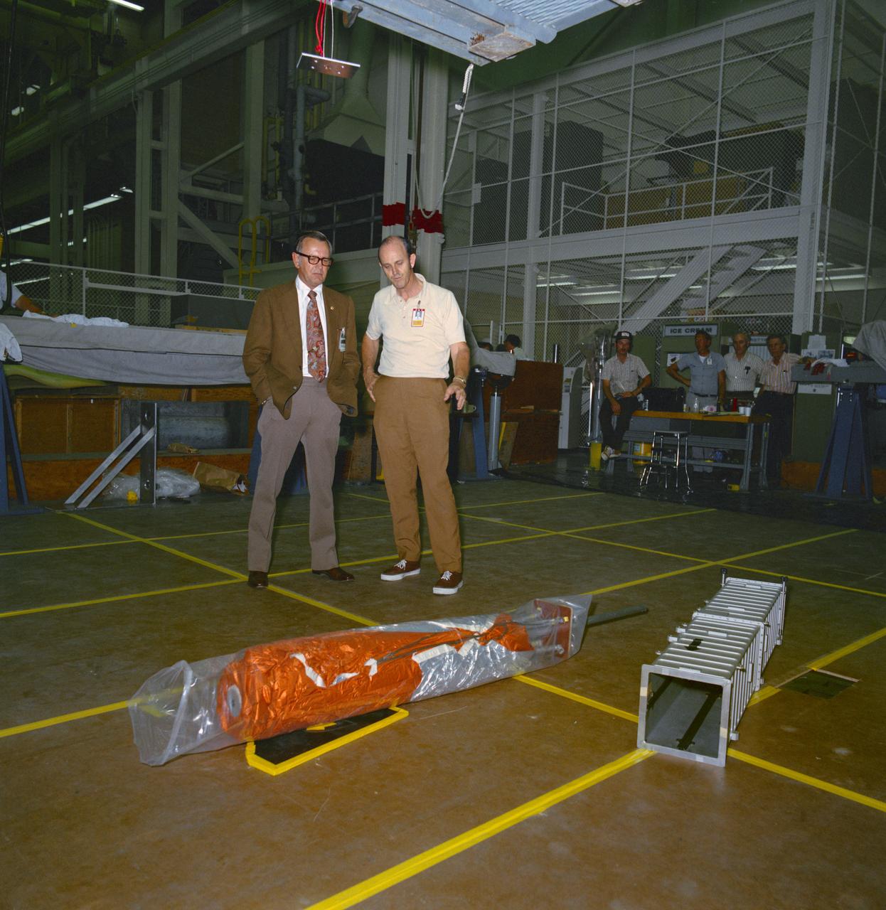 S73-26394 (23 May 1973) --- Dr. Christopher C. Kraft Jr. (left), JSC Director, and George A. Post, JSC Crew Systems Division, look over the packaged "parasol" during fabrication and checkout of the umbrella-like mechanical device in the Technical Services shop in building 10 at Johnson Space Center. The "parasol" is designed to fit into the T027 experiment photometer canister. The canopy portion of the "parasol" measures 24 feet by 22 feet. The "parasol" is one of several sunscreen possibilities being considered for use in shading the overheated Skylab 1 Orbital Workshop. Photo credit: NASA