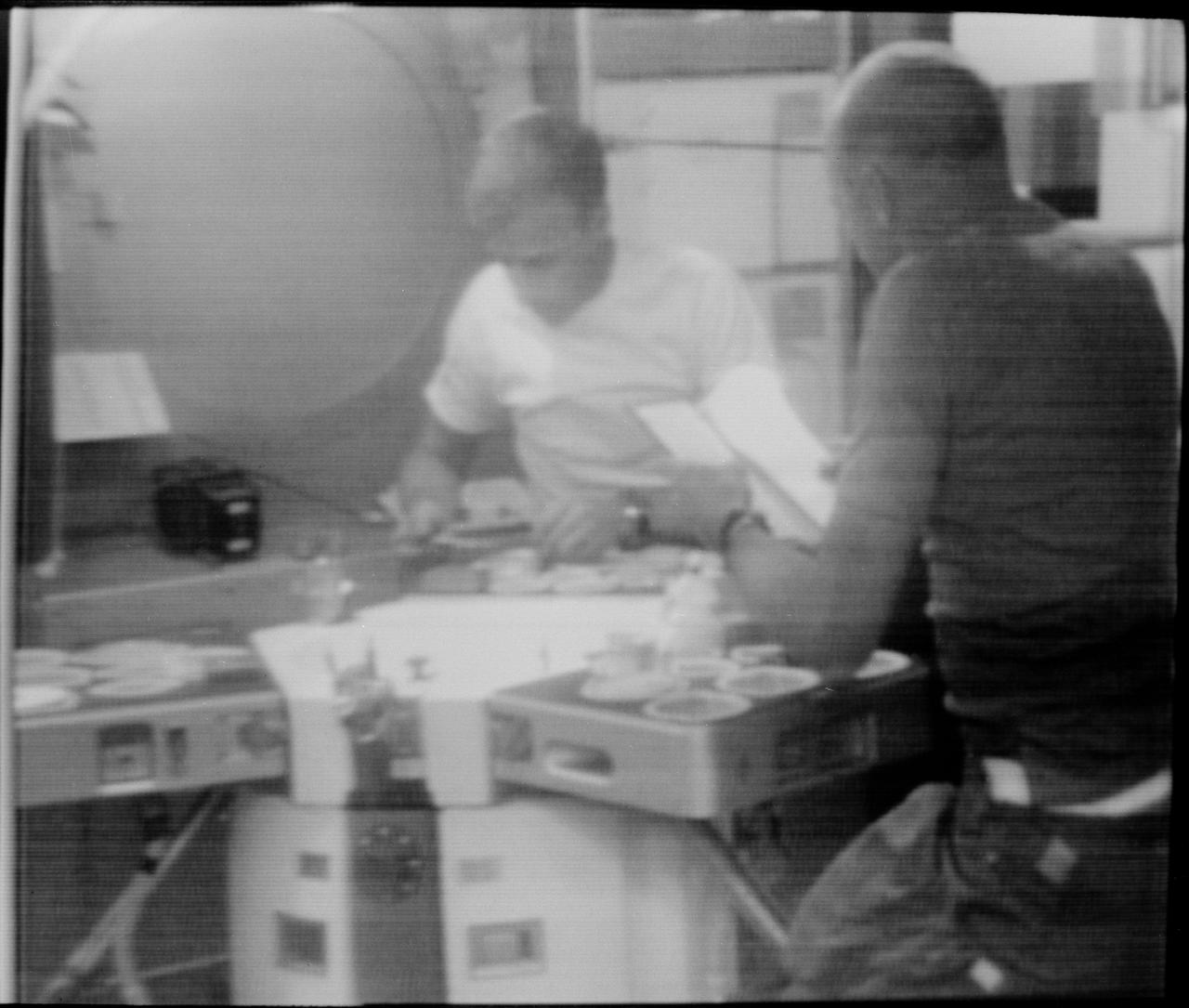 S73-27081 (30 May 1973) --- Two of the three Skylab 2 astronauts are seen in the wardroom of the crew quarters of the Orbital Workshop of the Skylab 1 space station cluster in Earth orbit in this reproduction taken from a television transmission made by a TV camera aboard the space station. They are preparing to eat a meal. Astronaut Charles Conrad Jr., commander, is in the right foreground. In the background is astronaut Paul J. Weitz, pilot. Photo credit: NASA