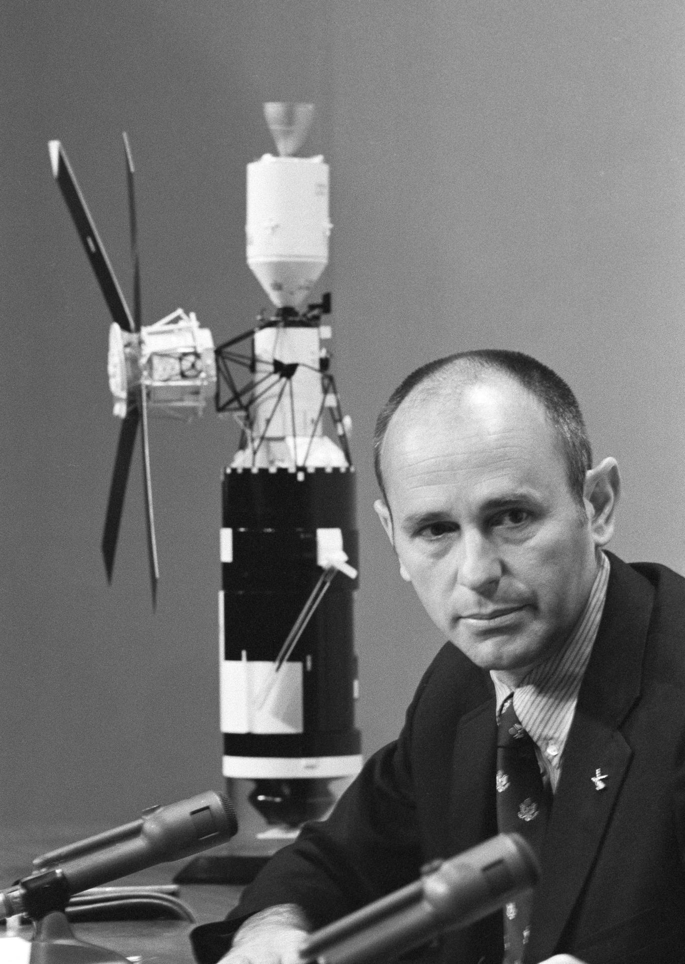 Al Bean speaks at a press conference with a model of the Skylab space station behind him