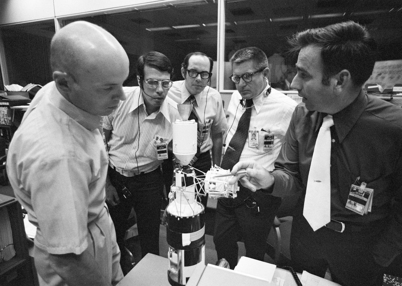 S73-31964 (5 August 1973) --- This group of flight controllers discuss today's approaching extravehicular activity (EVA) to be performed by the Skylab 3 crewmen. They are, left to right, scientist-astronaut Story Musgrave, a Skylab 3 spacecraft communicator; Robert Kain and Scott Millican, both of the Crew Procedures Division, EVA Procedures Section; William C. Schneider, Skylab Program Director, NASA Headquarters; and Milton Windler, flight director. Windler points to the model of the Skylab space station cluster to indicate the location of the ATM's film magazines. The group stands near consoles in the Mission Operations Control Room (MOCR) of the JSC Mission Control Center (MCC). Photo credit: NASA