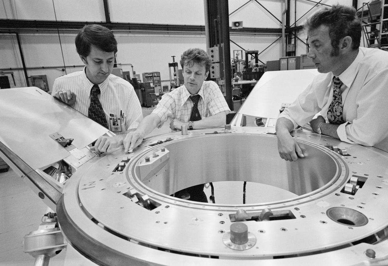 S74-24671 (10 July 1974) --- Three Apollo-Soyuz Test Project (ASTP) engineers look over a Soyuz spacecraft docking system prior to an ASTP docking mechanism fitness test conducted in Building 13 at the Johnson Space Center (JSC). They are (left to right) Robert White, Vladimir Syromyatnikov and Yevgeniy Bobrov.  White is the American chairman of ASTP Working Group Number 3, and Syromyatnikov is his Soviet counterpart. This working group is concerned with ASTP docking problems and procedures. White is with JSC's Spacecraft Design Division. Syromyatnikov is senior researcher of the Soviet State Research Institute of Machine Building. Bobrov is a junior researcher with the Institute of Machine Building. The joint United States - USSR ASTP docking mission in Earth orbit is scheduled for the summer of 1975.
