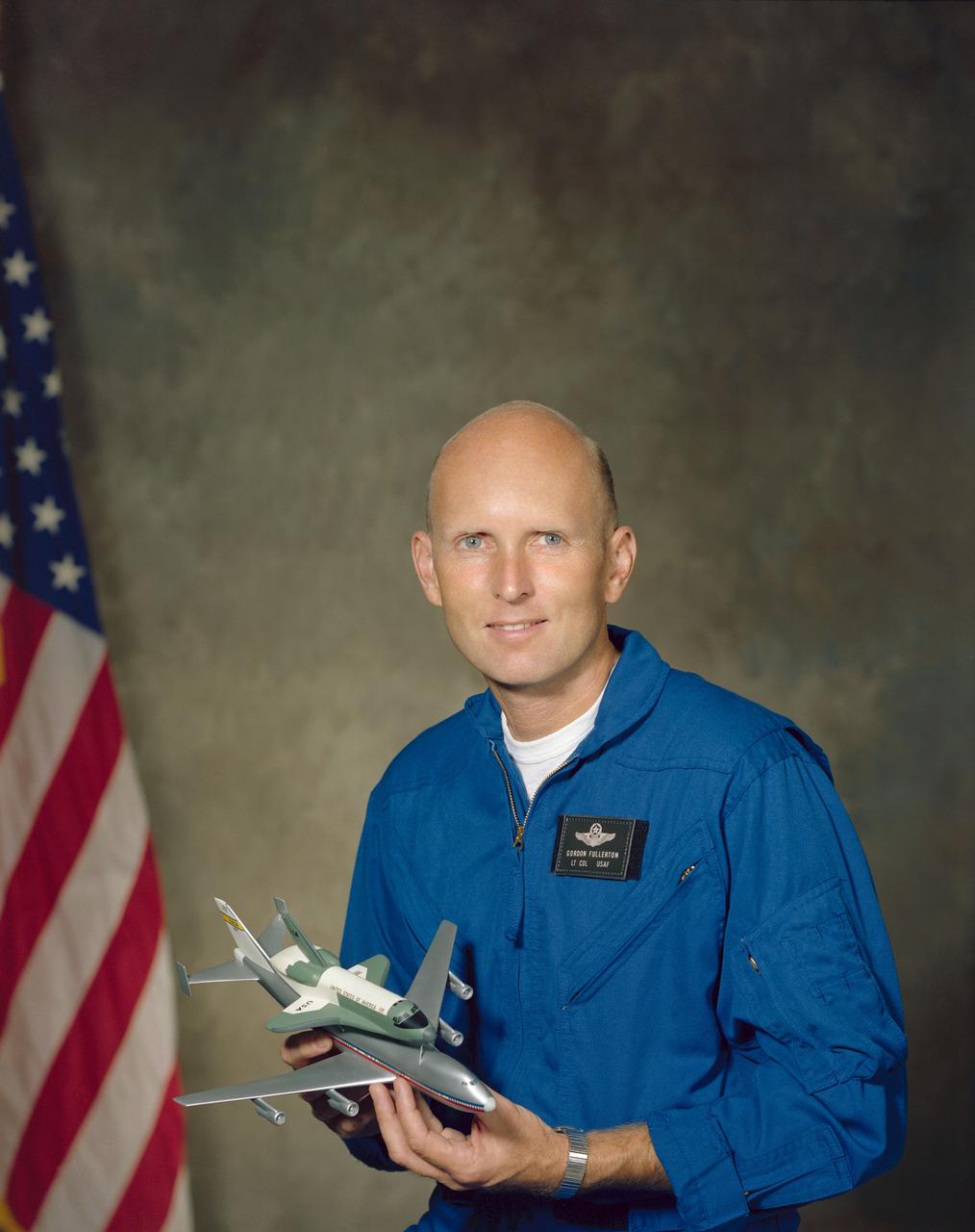 S76-28476 (8 Sept 1976) --- Astronaut C. Gordon Fullerton in flight suit holding a model of the space shuttle.