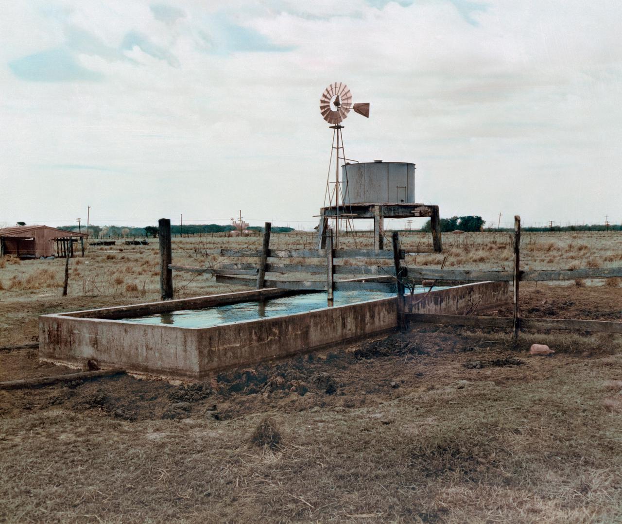 S76-32986 (March 1962) --- A color enhancement of a black and white photograph of a water trough, windmill, grazing area and feed lot on the future site of the Manned Spacecraft Center, Houston, Texas.    NOTE: The Manned Spacecraft Center was named Lyndon B. Johnson Space Center in memory of the late President following his death.