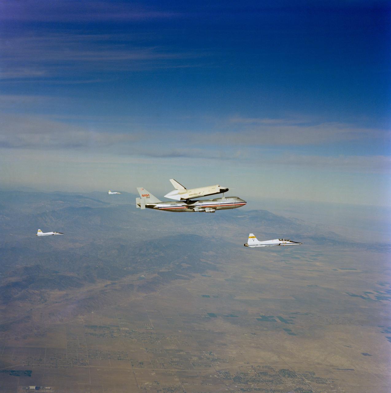 S77-28649 (23 Sept 1977) --- The shuttle Orbiter 101 "Enterprise" sits atop the NASA 747 carrier aircraft in a piggy-back configuration prior to separation for the third free flight of the Shuttle Approach and Landing Tests (ALT) conducted on September 23, 1977, at the Dryden Flight Research Center (DFRC) in Southern California. The crew of the "enterprise" consisted of astronauts Fred W. Haise Jr., commander, and C. Gordon Fullerton, pilot. This photo was shot from one of the T-38 chase planes accompanying the ALT craft. Three other T-38 chase planes are pictured.