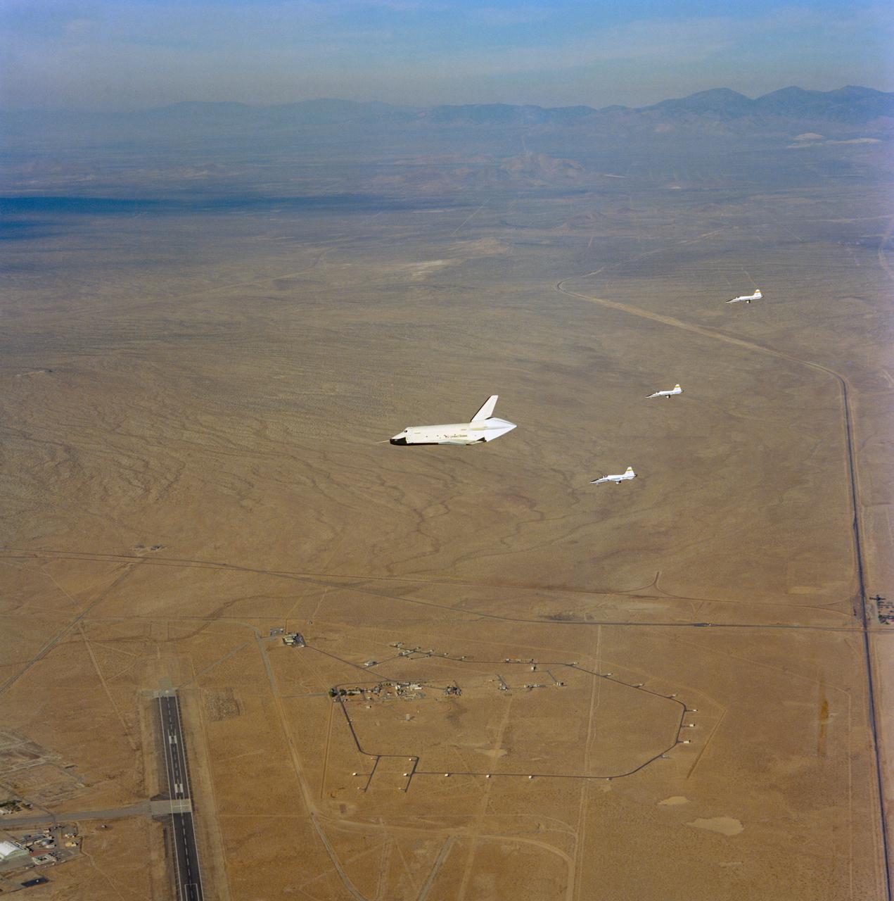 S77-28667 (23 Sept 1977) --- The shuttle Orbiter 101 "Enterprise" soars above the North Base area of Edwards Air Force Base during its five-minute, 34-second unpowered flight, the third of a series of manned Shuttle Approach and Landing Tests (ALT). Moments earlier the "Enterprise" had separated from its 747 carrier aircraft, atop which it sat upon takeoff from the Dryden Flight Research Center (DFRC), with its crew of astronauts Fred W. Haise Jr., commander, and C. Gordon Fullerton, pilot. Three T-38 chase planes follow. This photograph was taken from a fourth T-38 chase plane.