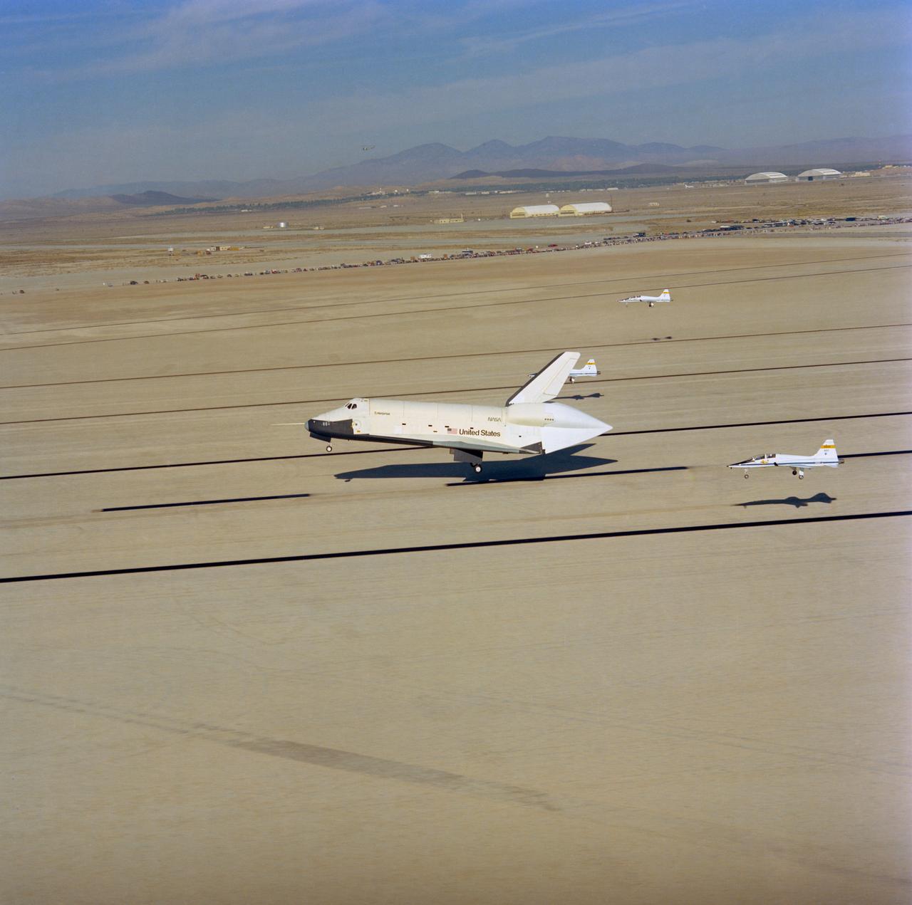 S77-28668 (23 Sept 1977) --- The shuttle Orbiter 101 "Enterprise" approaches touchdown on the runway at Edwards Air Force Base to conclude a five-minute, 34-second unpowered flight, the third of Shuttle Approach and Landing Tests (ALT) series, on September 23, 1977. Thress T-38 chase planes follow close by. Astronauts Fred W. Haise Jr., commander, and C. Gordon Fullerton, pilot, were the crew aboard the "Enterprise" for this flight.