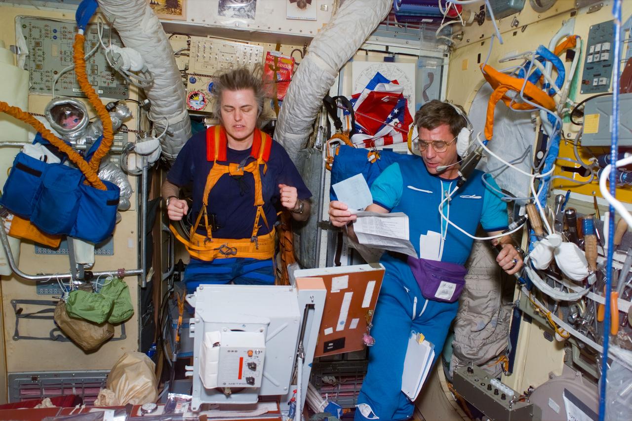 STS79-E-5145 (20 September 1996) --- Astronaut and cosmonaut guest researcher Shannon W. Lucid exercises on a treadmill while astronaut, soon-to-be cosmonaut guest researcher, John E. Blaha studies the daily planner, during Flight Day 5.
