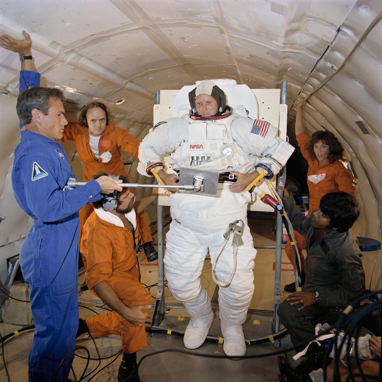 S81-34432 (July 1981) --- Astronaut C. Gordon Fullerton, STS-3 pilot, takes part in a suit donning and doffing exercise aboard a KC-135 "zero-gravity" aircraft. Mission specialist/astronaut William F. Fisher holds a mirror to assist Fullerton with hose and cable linkups to his suit. A special parabolic pattern flown by the KC-135 provides short durations of weightlessness. Fullerton's suit is an Extravehicular Mobility Unit (EMU), used by astronauts when leaving the shirt-sleeve environment of their shuttle orbiter to go outside and perform tasks in the vacuum of space. There are no such EVA plans on STS-3, but the crewmen are trained in this area in the event of a contingency. Photo credit: NASA