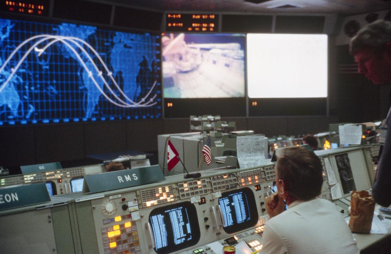 S81-39494 (12 Nov. 1981) --- An overall view of activity in the mission operations control room (MOCR) in Houston?s Mission Control Center (MCC) as viewed from the second front row of consoles during the STS-2 mission. The remote manipulator system (RMS) console is in the immediate foreground. Note TV transmission on the Eidophor screen at front of MOCR and shuttle orbiter marker on tracking map at left indicating the vehicle?s location over the Hawaiian Islands. The downlink was through the Hawaii tracking station. Photo credit: NASA