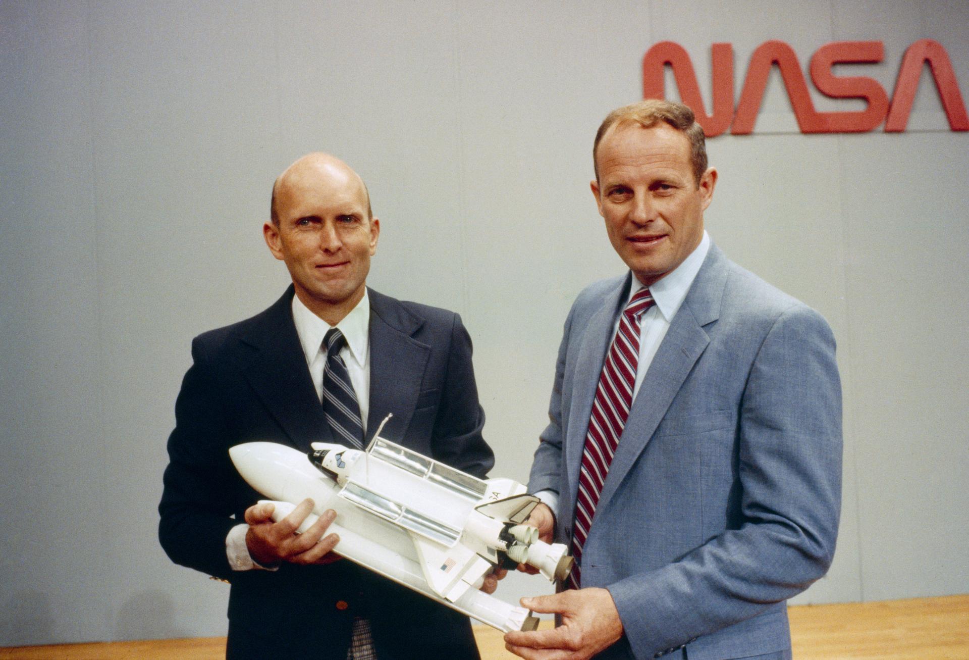 Jack Lousma and Gordon Fullerton pose with a model of the Space Shuttle