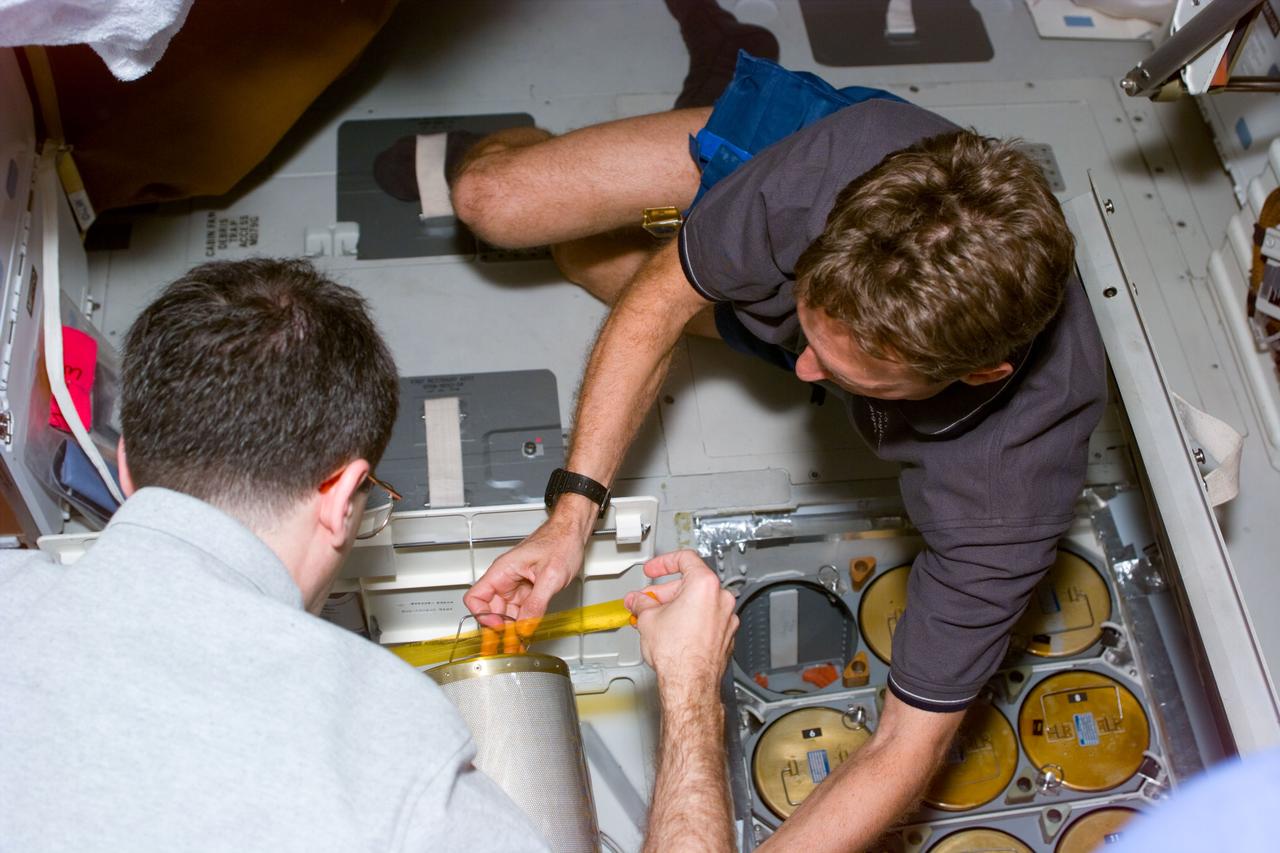 STS081-E-5007 (12 Jan. 1997) --- Astronauts Peter J. K. (Jeff) Wisoff (left) and Jerry M. Linenger begin early housekeeping by putting in fresh lithium hydroxide canisters beneath the Space Shuttle Atlantis' middeck. Not far away in Atlantis' cargo bay, the two mission specialists and their four crew mates are flying the Spacehab Double Module (DM), replete with supplies for the three-man crew aboard Russia's Mir Space Station with which Atlantis will be docking later in the week. Linenger will trade places with John E. Blaha, marking the second such exchange of American astronaut - cosmonaut guest researcher's aboard Mir. Blaha had replaced Shannon W. Lucid in September of 1996. The scene was recorded with an Electronic Still Camera (ESC) and later downlinked to flight controllers in Houston, Texas.