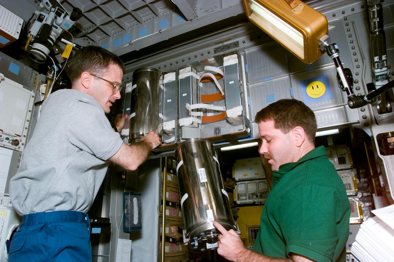 STS081-E-05094 (12 Jan. 1997) --- Astronauts Peter J. K. (Jeff) Wisoff (left) and John M. Grunsfeld, mission specialists, deploy two Passive Thermal Conditioning Units (PTCU) onboard the SPACEHAB Double Module (DM) late on Day 1 of the mission. The two units had been transported by the pair through the tunnel connecting SPACEHAB and the mid-deck of crew cabin of the Space Shuttle Atlantis. They are joined by four other NASA astronauts for the almost ten-day mission. The crew is scheduled to dock with Russia's Mir Space Station and pick up John E. Blaha, NASA astronaut who has been serving as a cosmonaut guest researcher since September 1996. Jerry M. Linenger (out of frame) will replace Blaha onboard Mir.