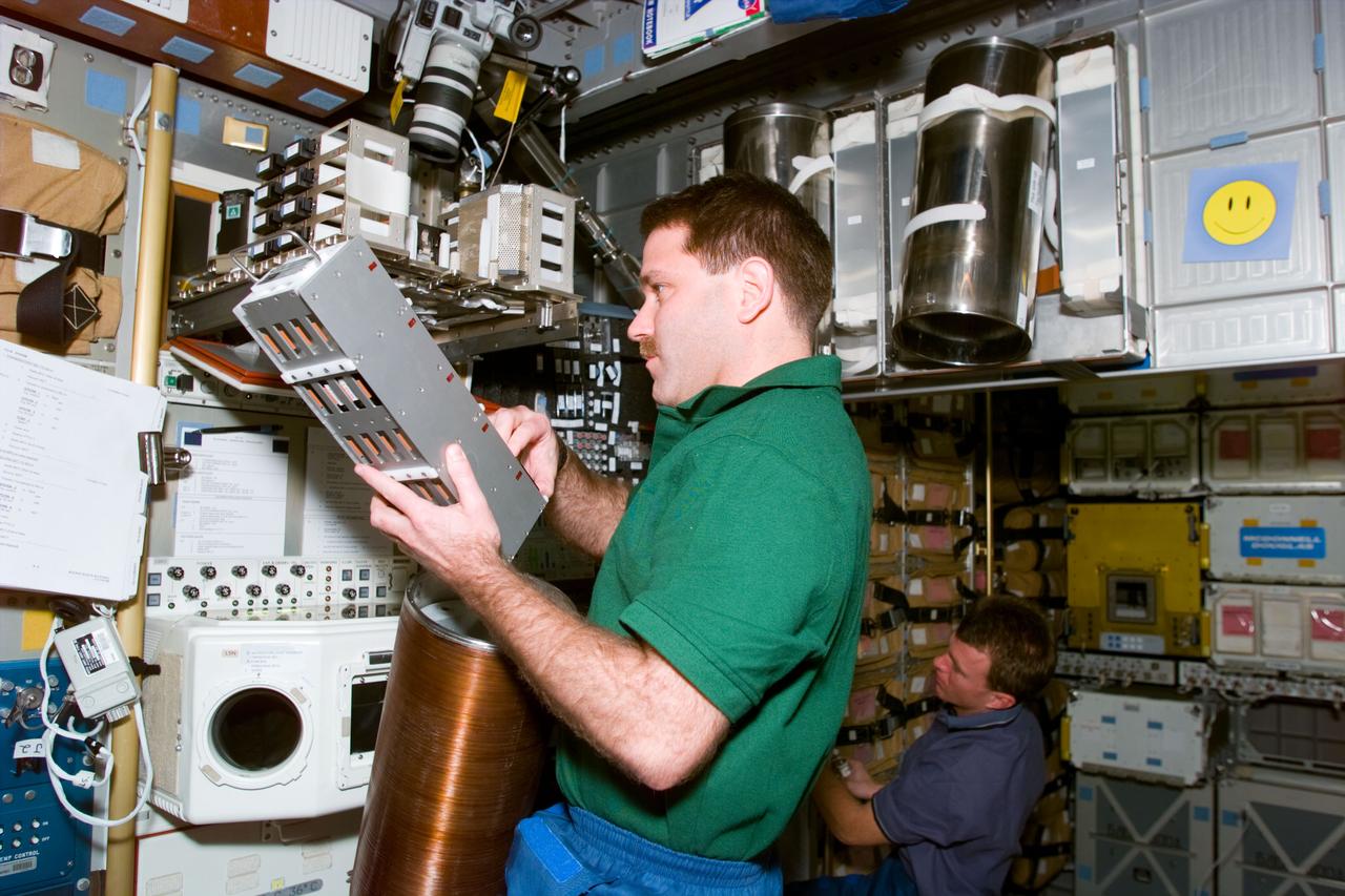 STS081-E-05145 (13 Jan. 1997) --- Astronaut John M. Grunsfeld, mission specialist, works with a Passive Thermal Conditioning Unit (PTCU), the cylindrical device suspended between the mission specialist and the nearby biorack glovebox onboard the Spacehab Double Module (DM). He holds a container of experiment samples in his left hand. This image was recorded with an Electronic Still Camera (ESC) and was later downlinked to flight controllers in Houston, Texas. Grunsfeld and five astronaut crew mates are preparing for a scheduled mid-week docking with Russia's Mir Space Station.