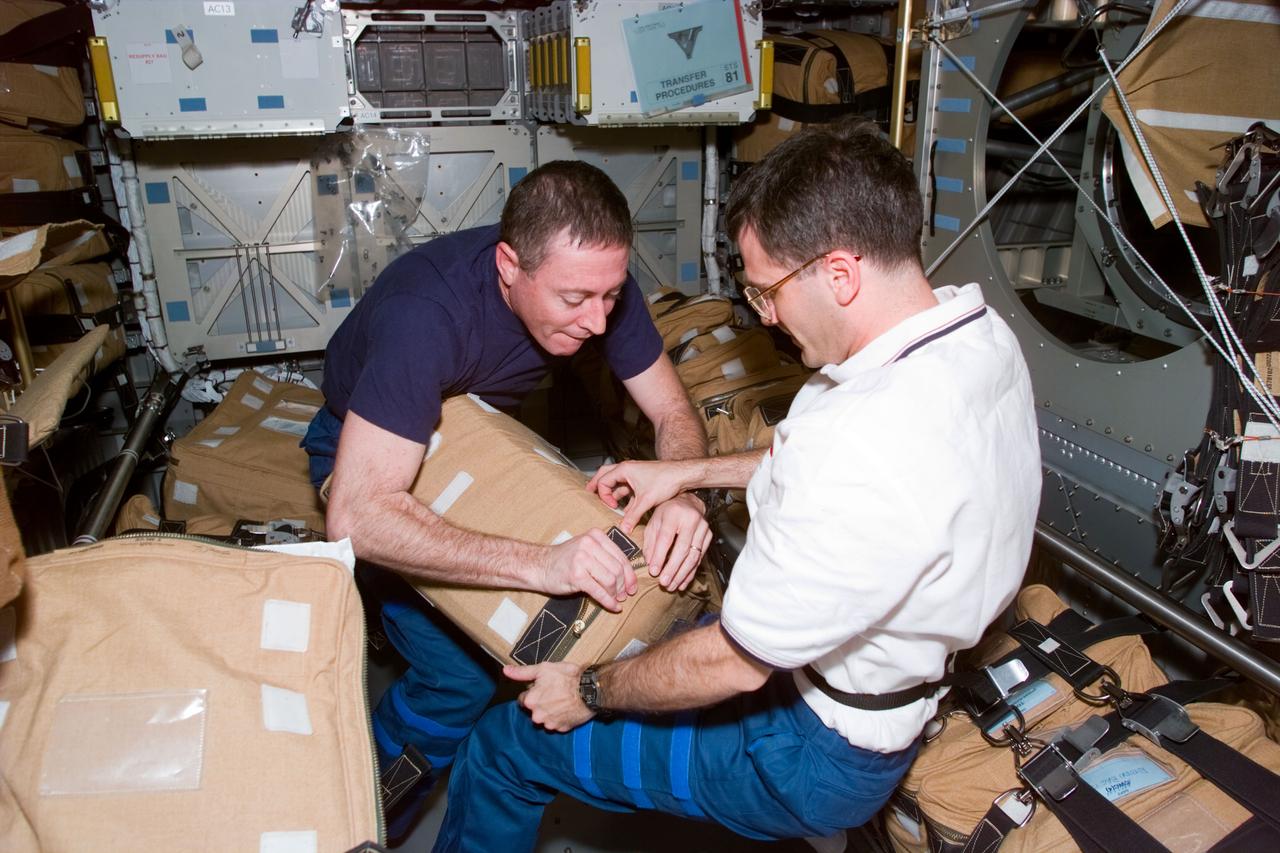 STS081-E-05515 (16 Jan. 1997) --- Astronauts Michael A. Baker, commander, and Peter J. K. (Jeff) Wisoff, mission specialist, secure a bag filled with a drawer of supplies in the Spacehab Double Module (DM). The scene was recorded with an Electronic Still Camera (ESC) and later downlinked to flight controllers in Houston, Texas.