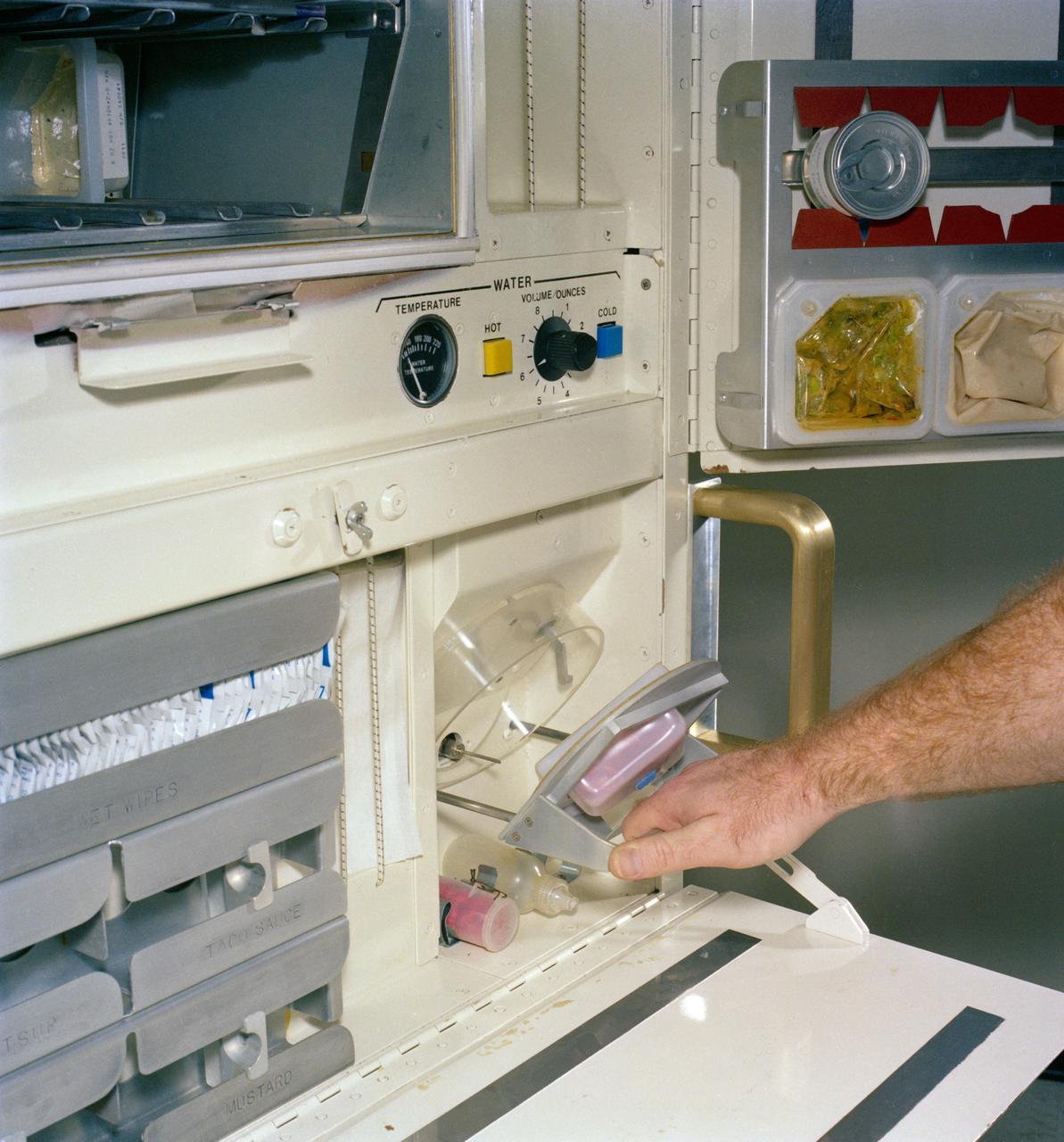 S82-26423 (January 1982) --- This is a close-up view of the rehydration unit to be used in meal preparation on operational space shuttle flights.  The unit is located on the middeck of the space shuttles in the NASA fleet. Note the part of the food tray in upper right corner. Its six compartments (not all pictured) are used in space shuttle meal preparation and consumption.  Photo credit: NASA