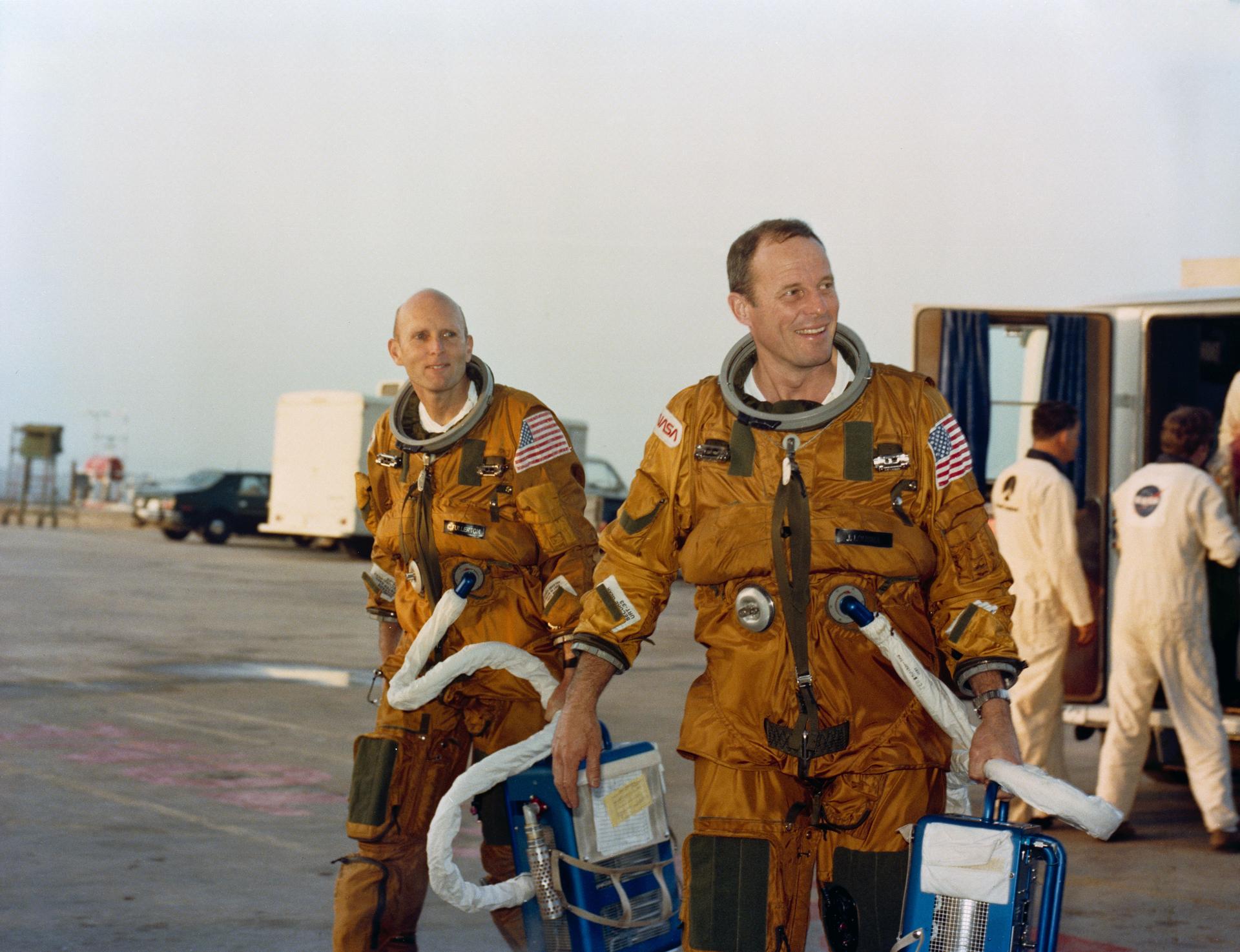 Astronaut Jack R. Lousma, right, STS-3 commander, and C. Gordon Fullerton, pilot (left), carry portable spacesuit air controllers as they walk from a transport van to Launch Pad 39A to participate in a simulated countdown and launch.