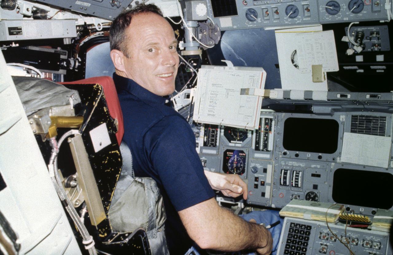 S82-28907 (March 1982) --- Astronaut Jack R. Lousma turns toward astronaut C. Gordon Fullerton and smiles into the lens of the 35mm camera Fullerton used to expose this frame onboard the busy Earth-orbiting space shuttle Columbia. Lousma is at the commander's station of the forward flight deck on the Columbia.  His front window view is of Earth below (note river upper right center). Lousma is wearing the trouser and shirt of a three-piece (jacket temporarily not worn) constant-wear garment.  Except for entry and launch phases, shuttle crews wear the CWG throughout their awake hours. A data acquisition camera (DAC) is at upper left, along with a TV camera. Photo credit: NASA
