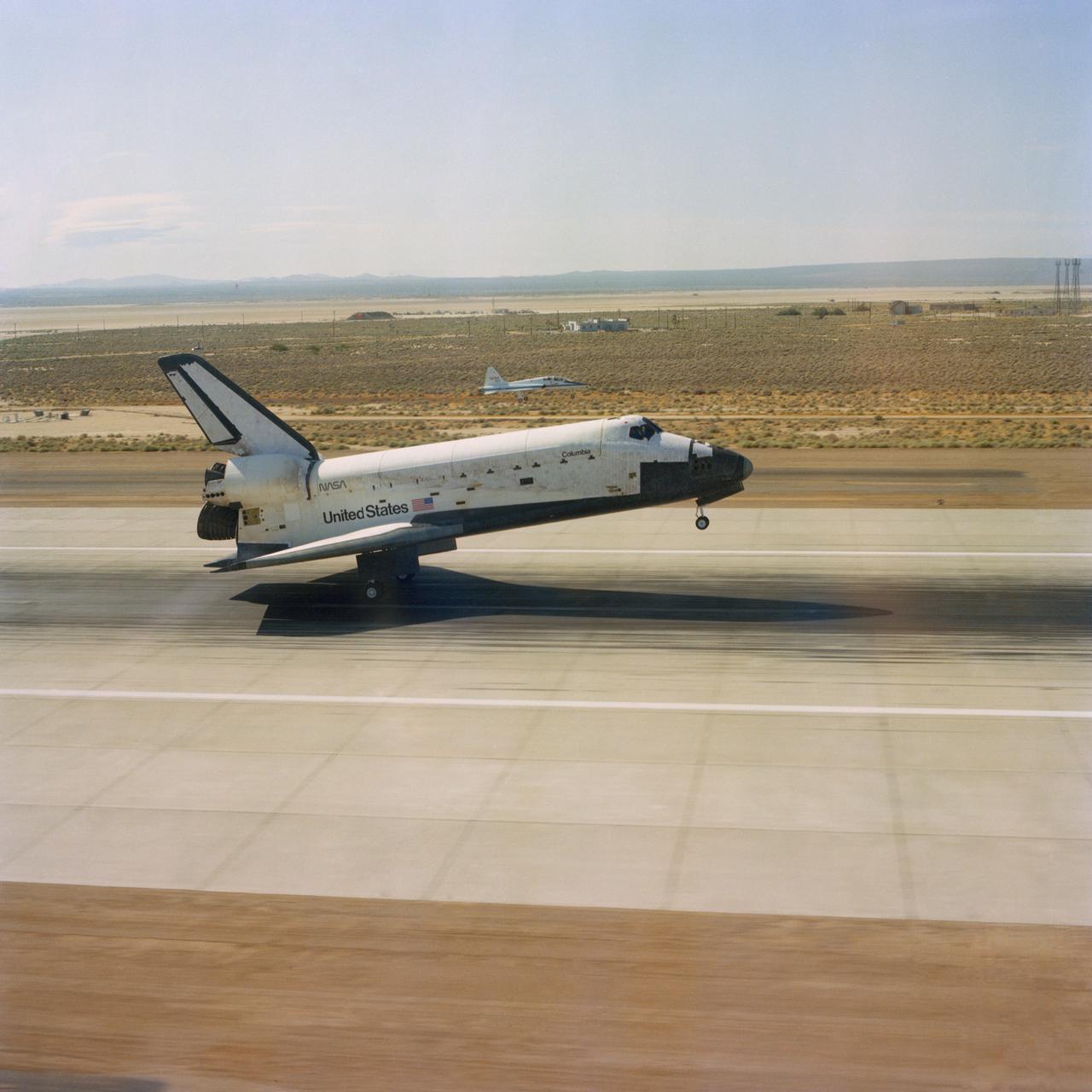 S82-33420 (4 July 1982) --- The aft wheels of the space shuttle Columbia ease down on the runway at Edwards Air Force Base (AFB) today to successfully complete a week-long spaceflight for astronauts Thomas K. Mattingly II, and Henry W. Hartsfield Jr. A T-38 aircraft serves as a chase plane (just above center of photo) in the background. Not long after this photograph was made and the crew had egressed their craft, President Ronald Reagan addressed a giant crowd on hand at Edwards AFB for a special kind of July 4 celebration. Photo credit: NASA