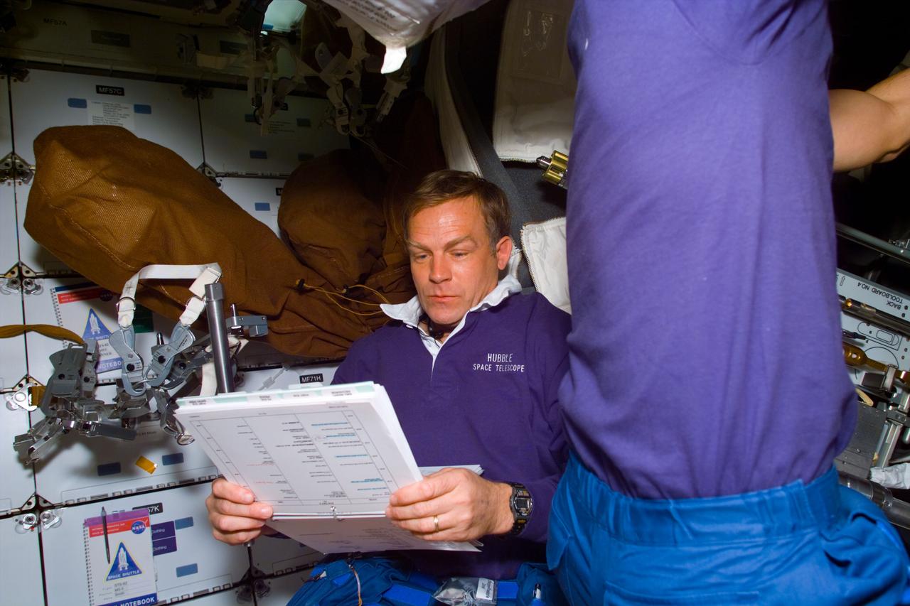 S82-E-5002 (12 Feb. 1997) --- On the Space Shuttle Discovery's middeck, STS-82 payload commander Mark C. Lee looks over plan for the first space Extravehicular Activity (EVA) as an unidentified crew mate (right) unstows a piece of related gear. Four of the crew members will perform a series of EVA's to service the Hubble Space Telescope (HST).  This photograph (as well as the others in this series) was recorded with an Electronic Still Camera (ESC) late during Discovery's first full day in orbit and downlinked later to flight controllers in Houston, Texas.