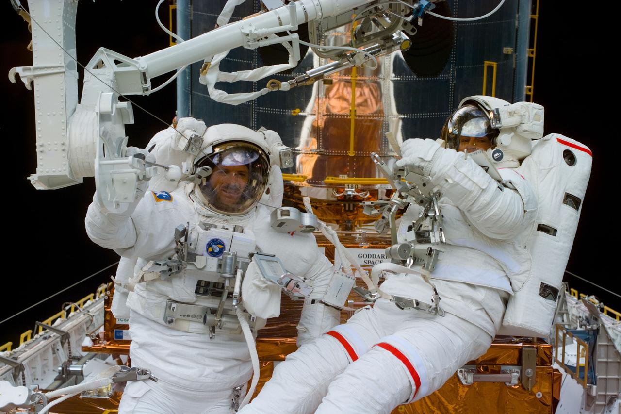 S82-E-5572 (16 Feb. 1997) --- Pausing near the foot-restraint of the Remote Manipulator System (RMS), astronauts Steven L. Smith (left) and Mark C. Lee communicate with and look toward their in-cabin team members during the third Extravehicular Activity (EVA) to perform servicing chores on the Hubble Space Telescope (HST).  This view was taken with an Electronic Still Camera (ESC).